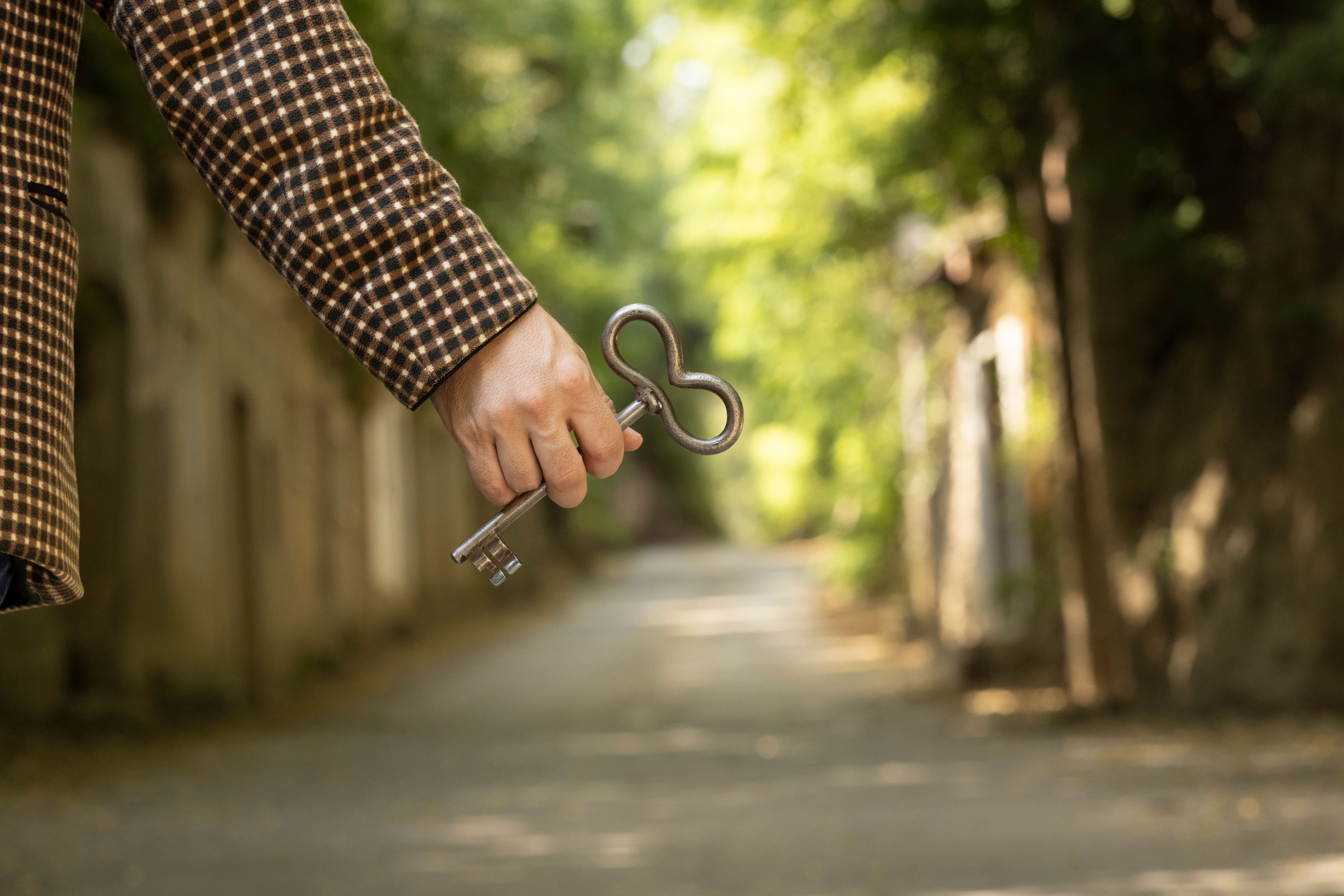 Eine Hand hält einen Kellerschlüssel, im Hintergrund ist eine Hohlwegkellergasse sichtbar.