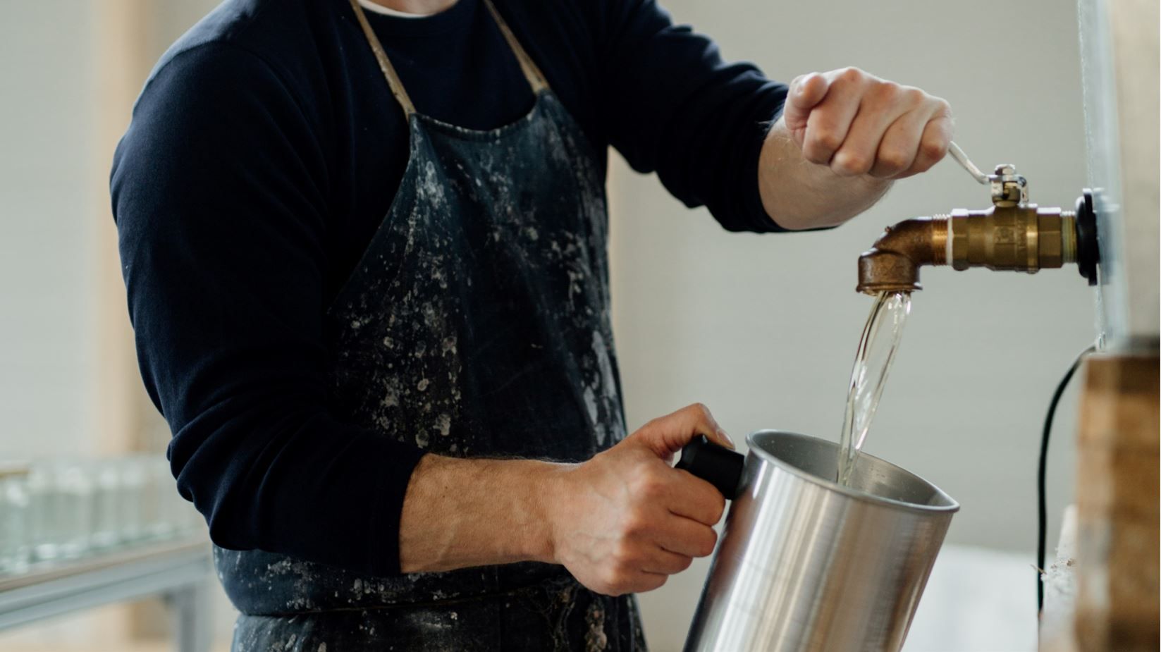 Person füllt Wasser aus einem Hahn in einen Metallbehälter.