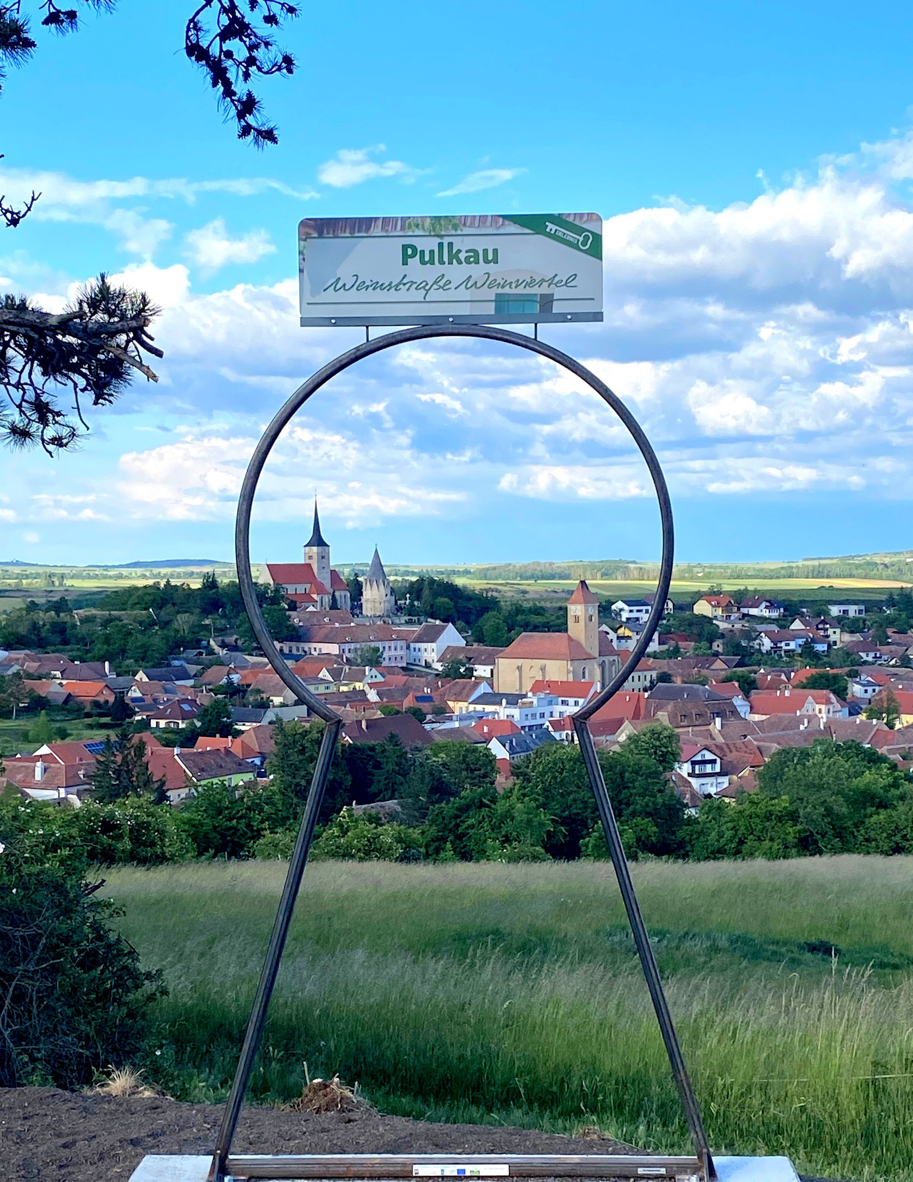 Blick auf Pulkau durch einen Metallrahmen mit Schild 'Weinstraße Weinviertel'.
