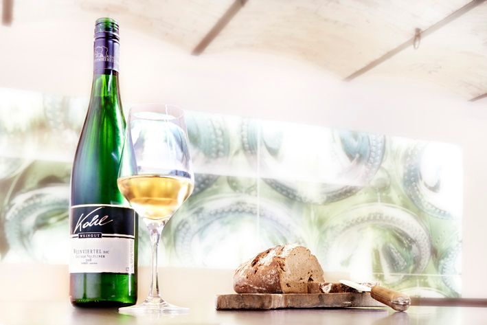 Eine Flasche Weißwein, ein gefülltes Weinglas und ein Laib Brot auf einem Tisch.