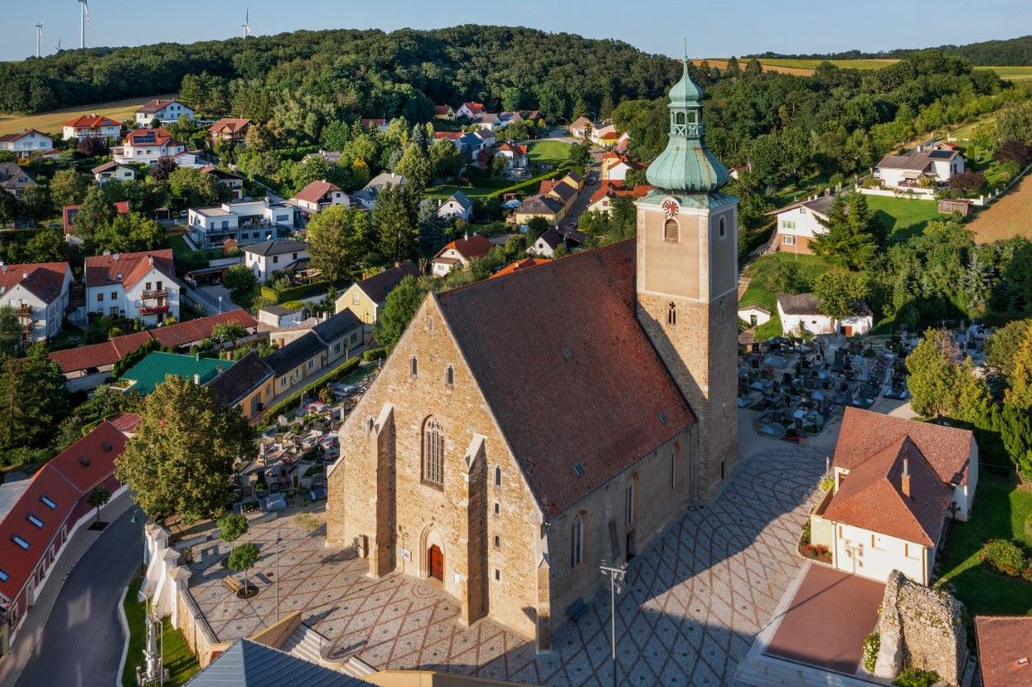 Letecký pohled na kostel ve vesnici s okolními domy a hřbitovem.