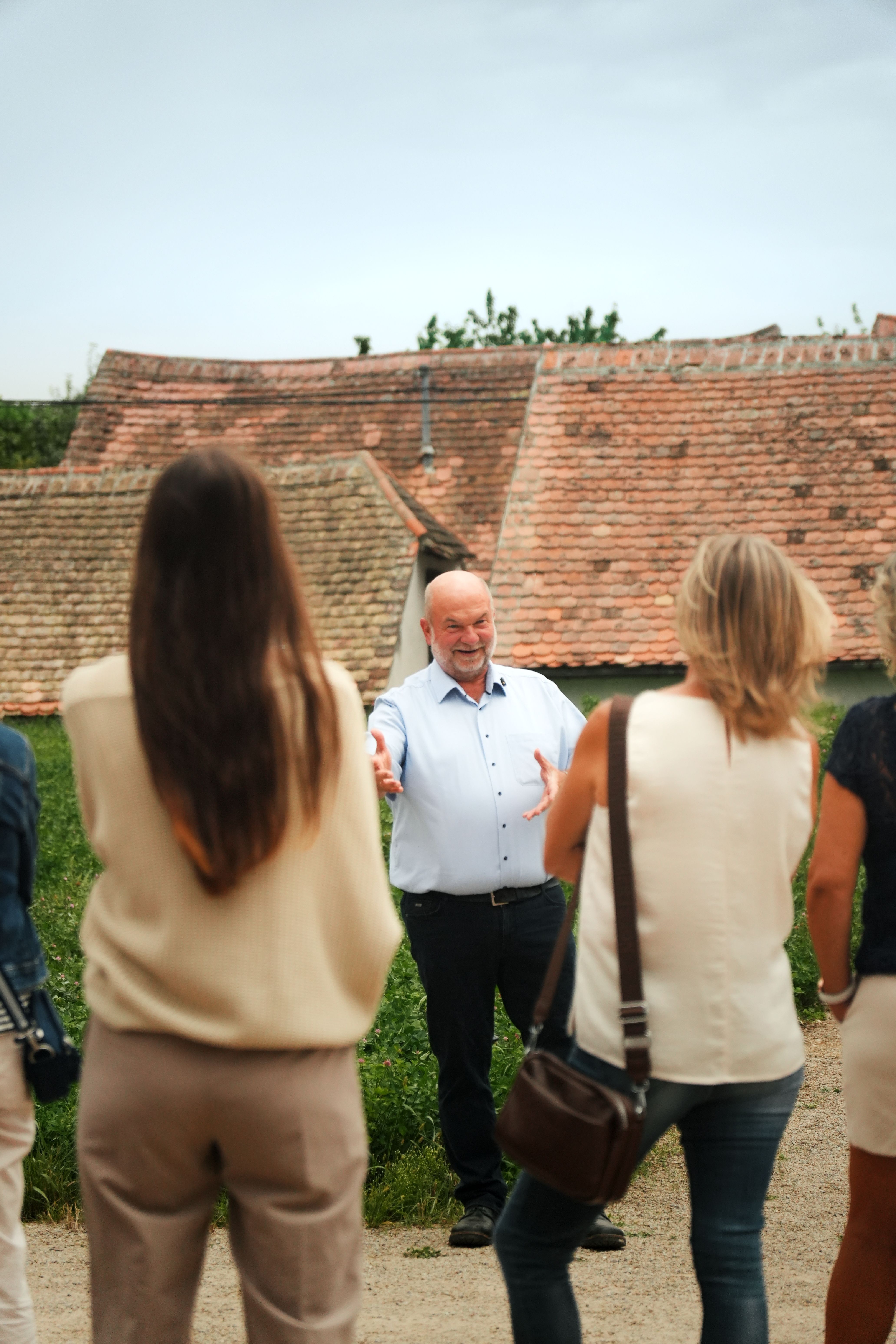 Ein Mann steht umgeben von einer Gruppe Personen und erklärt stark gestikulierend etwas, im Hintergrund sieht man Dächer von Presshäusern.