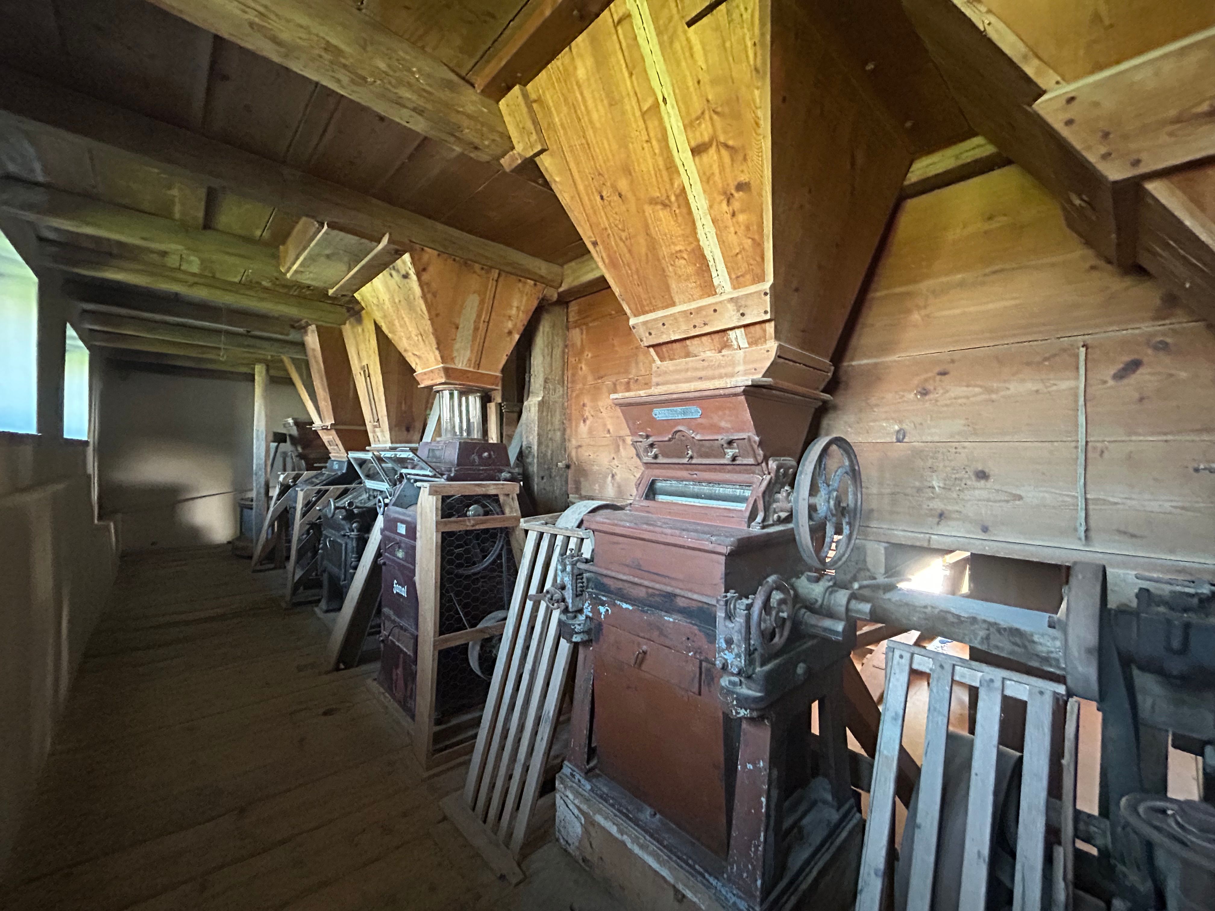 Innenansicht einer alten Mühle mit hölzernen Getreidebehältern und Maschinen.