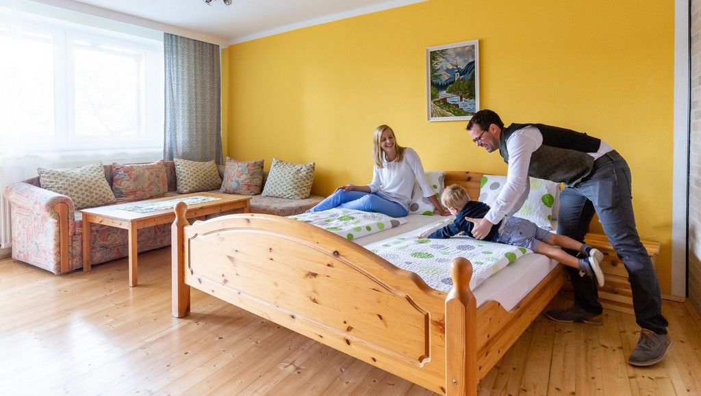 Ein gemütliches Zimmer mit gelber Wand, einem Holzbett und einer Familie, die auf dem Bett spielt.