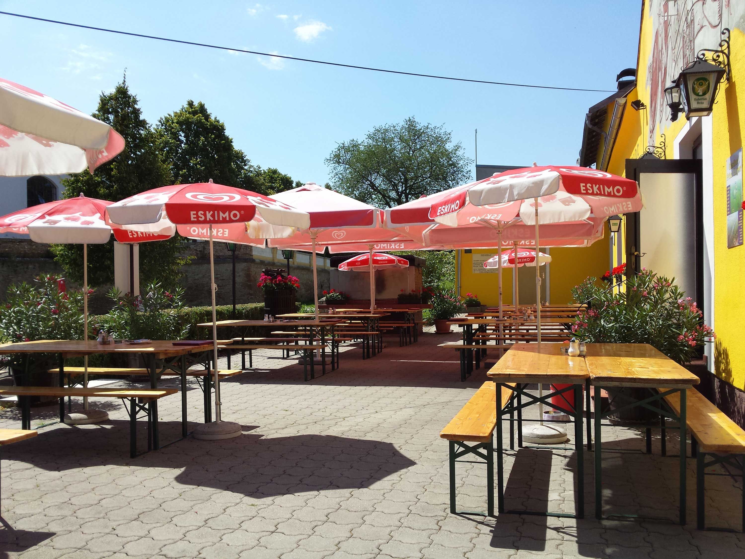 Sunny terrace with wooden benches and red parasols.