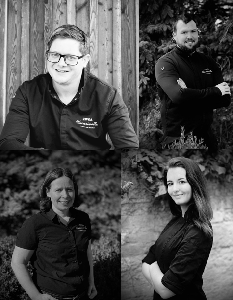 Vier Personen in Schwarz-Weiß-Porträts, die lächeln und in Arbeitskleidung posieren.