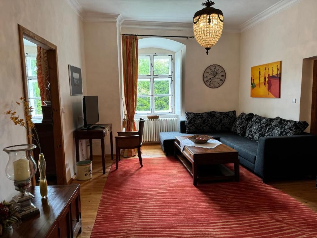 Gemütliches Wohnzimmer mit Sofa, rotem Teppich, Kronleuchter und großem Fenster.