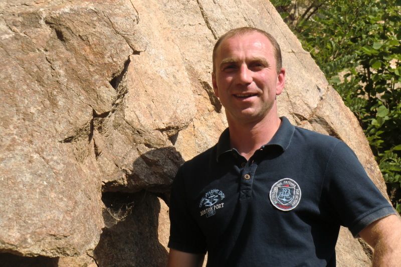 Ein Mann steht vor einem großen Felsen und lächelt in die Kamera.