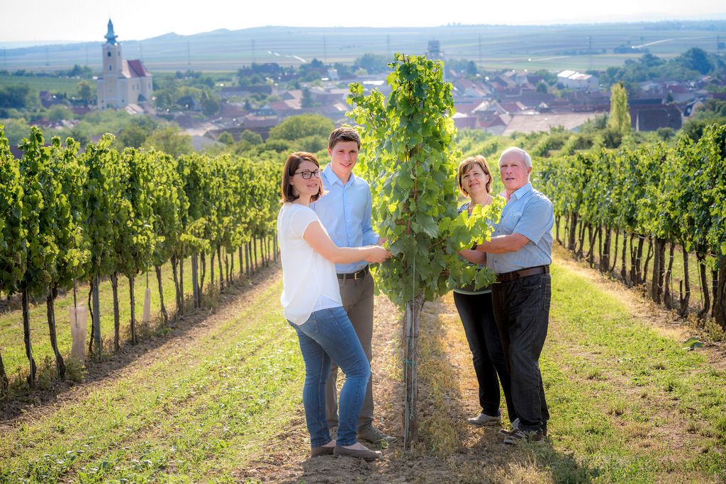 Eine Winzerfamilie steht in einem Weinberg mit einer Kirche im Hintergrund.