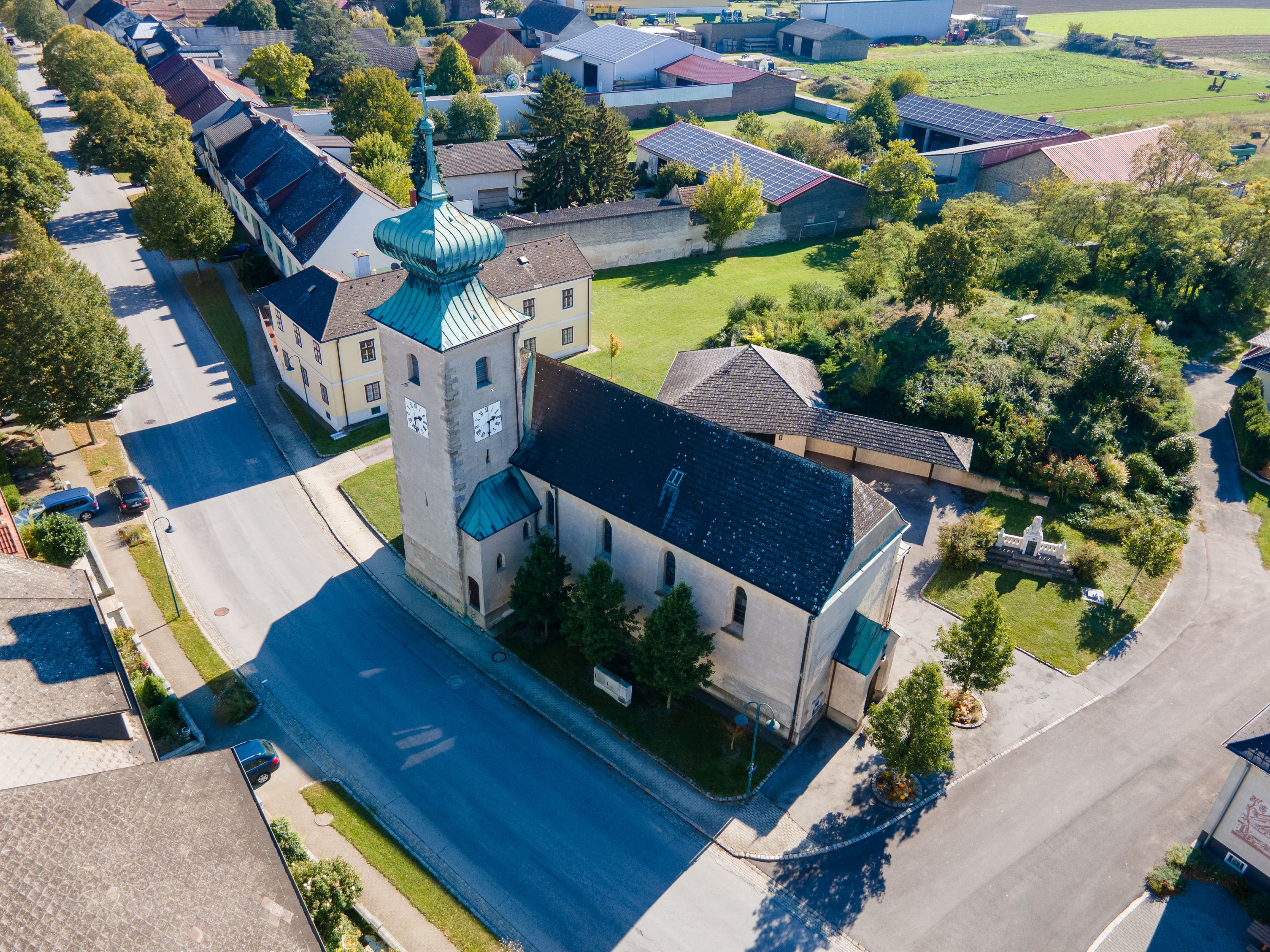 Luftaufnahme der Kirche in der Gemeinde Weiden an der March mit Turm, Kupferdach und umliegenden Häusern und Gärten.