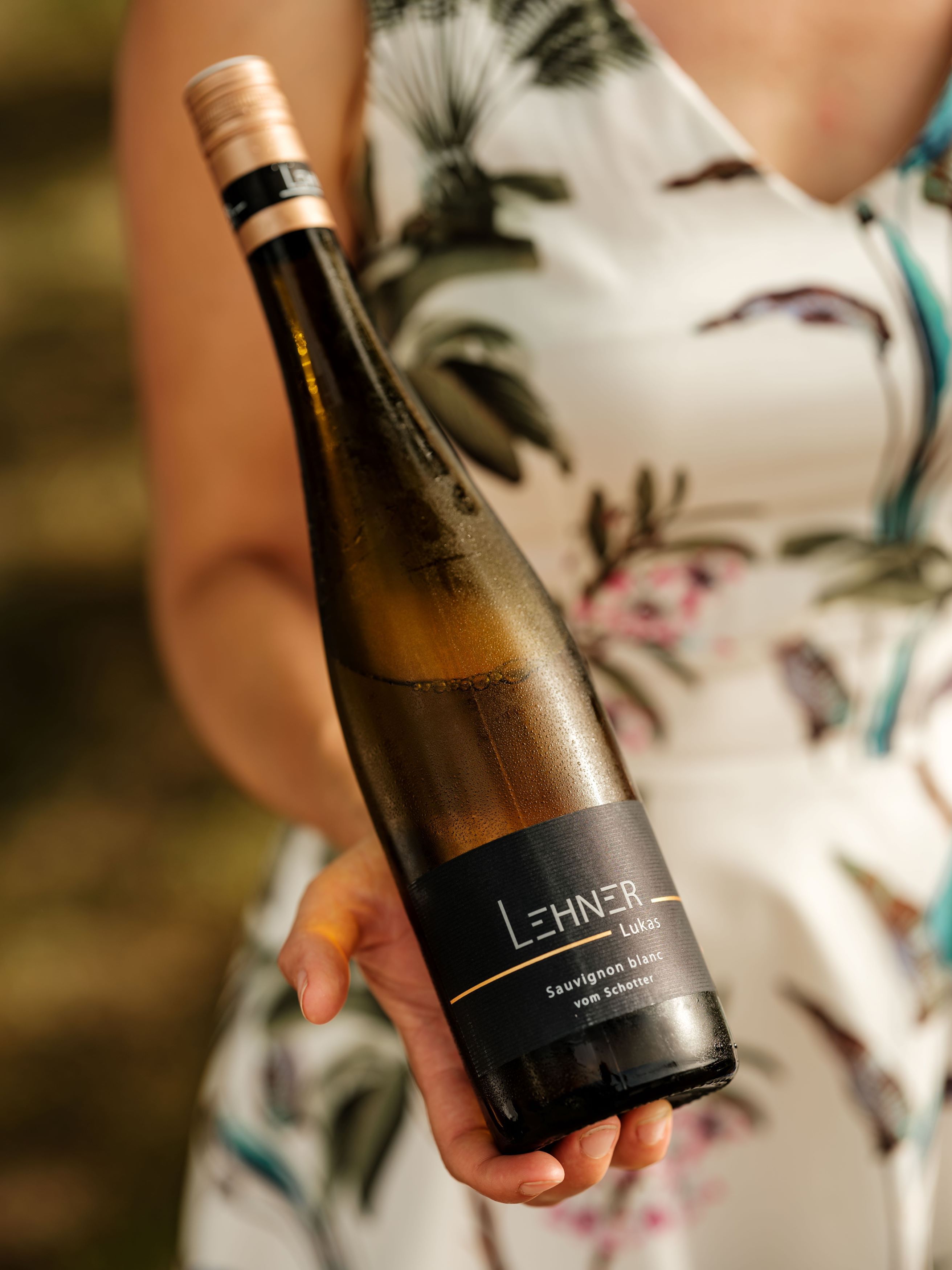 One person is holding a bottle of wine with the label 'Lehner Lukas Sauvignon blanc vom Schotter'.