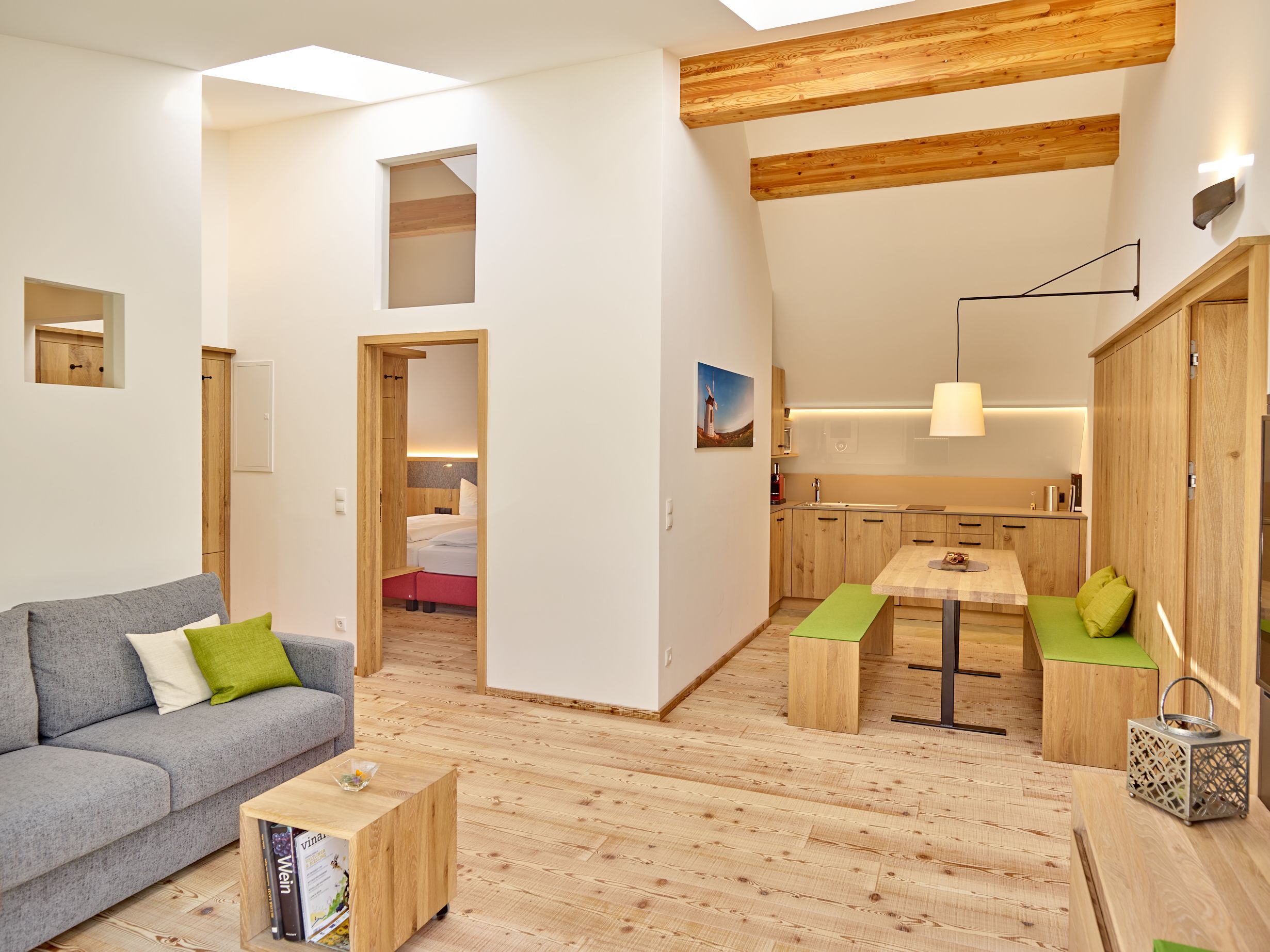 Modernes Wohnzimmer mit Holzmöbeln, grauem Sofa und offener Küche.