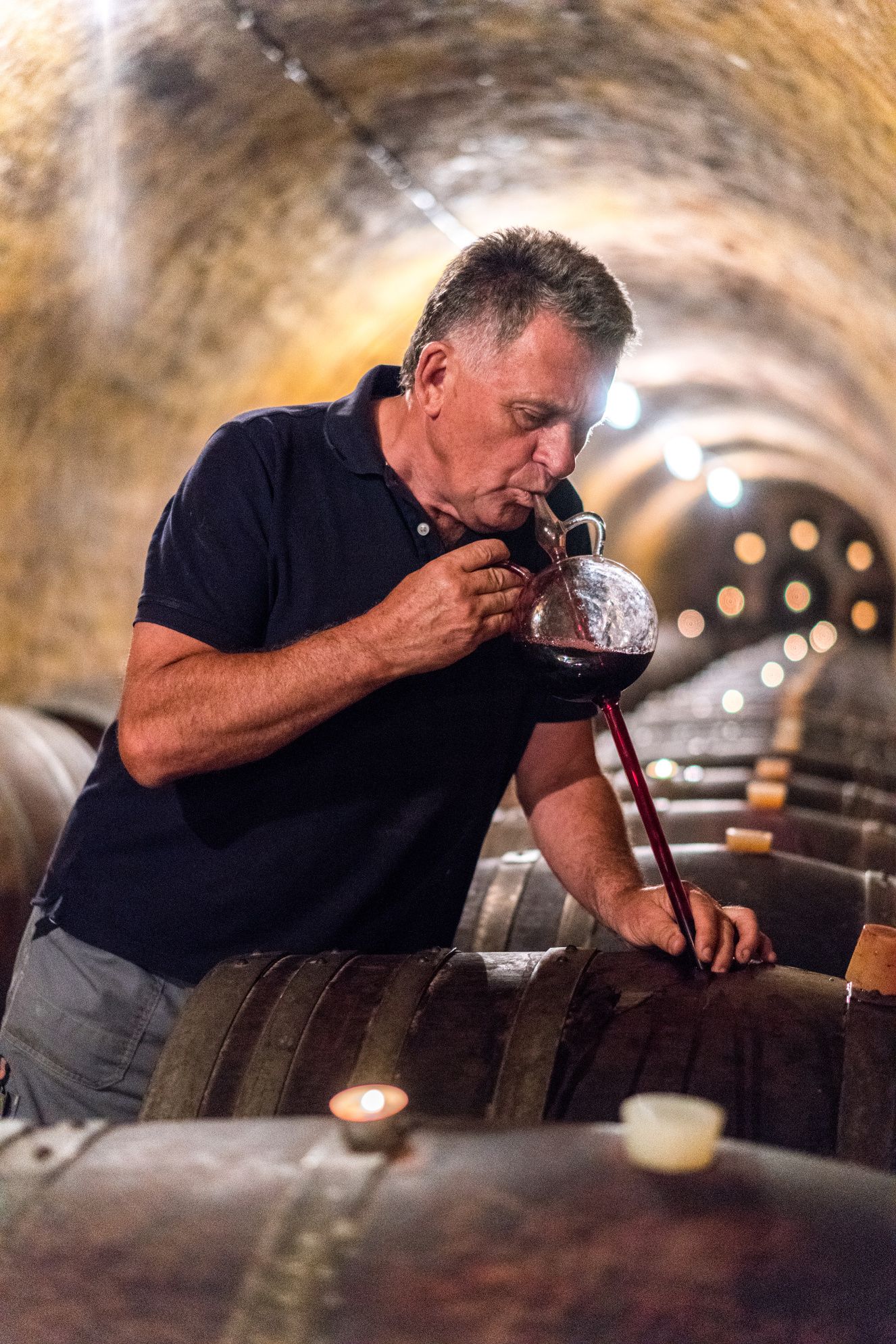 Ein Mann probiert Wein aus einem Fass in einem Weinkeller.