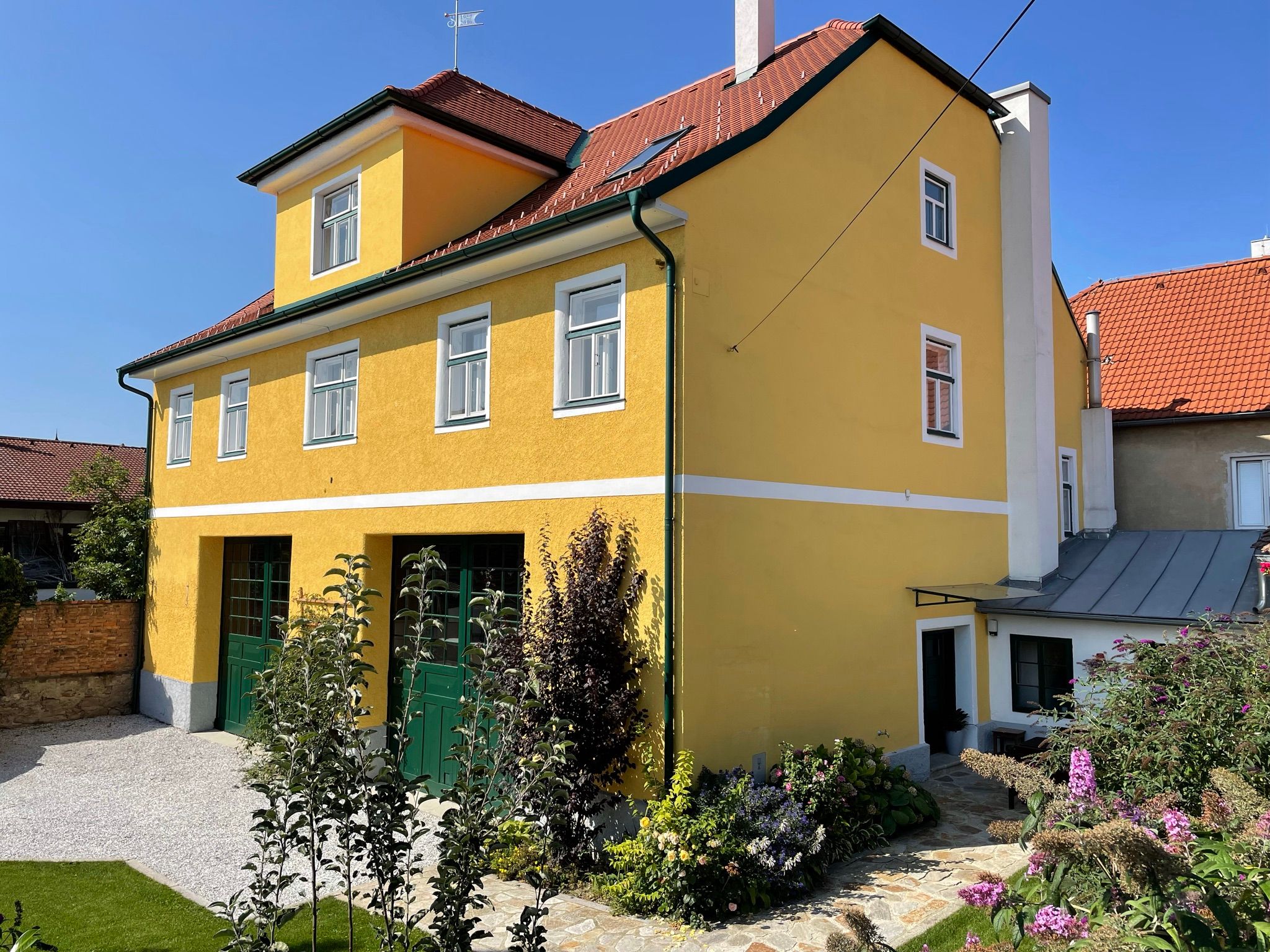 Gelbes zweistöckiges Haus mit rotem Dach und Garten.