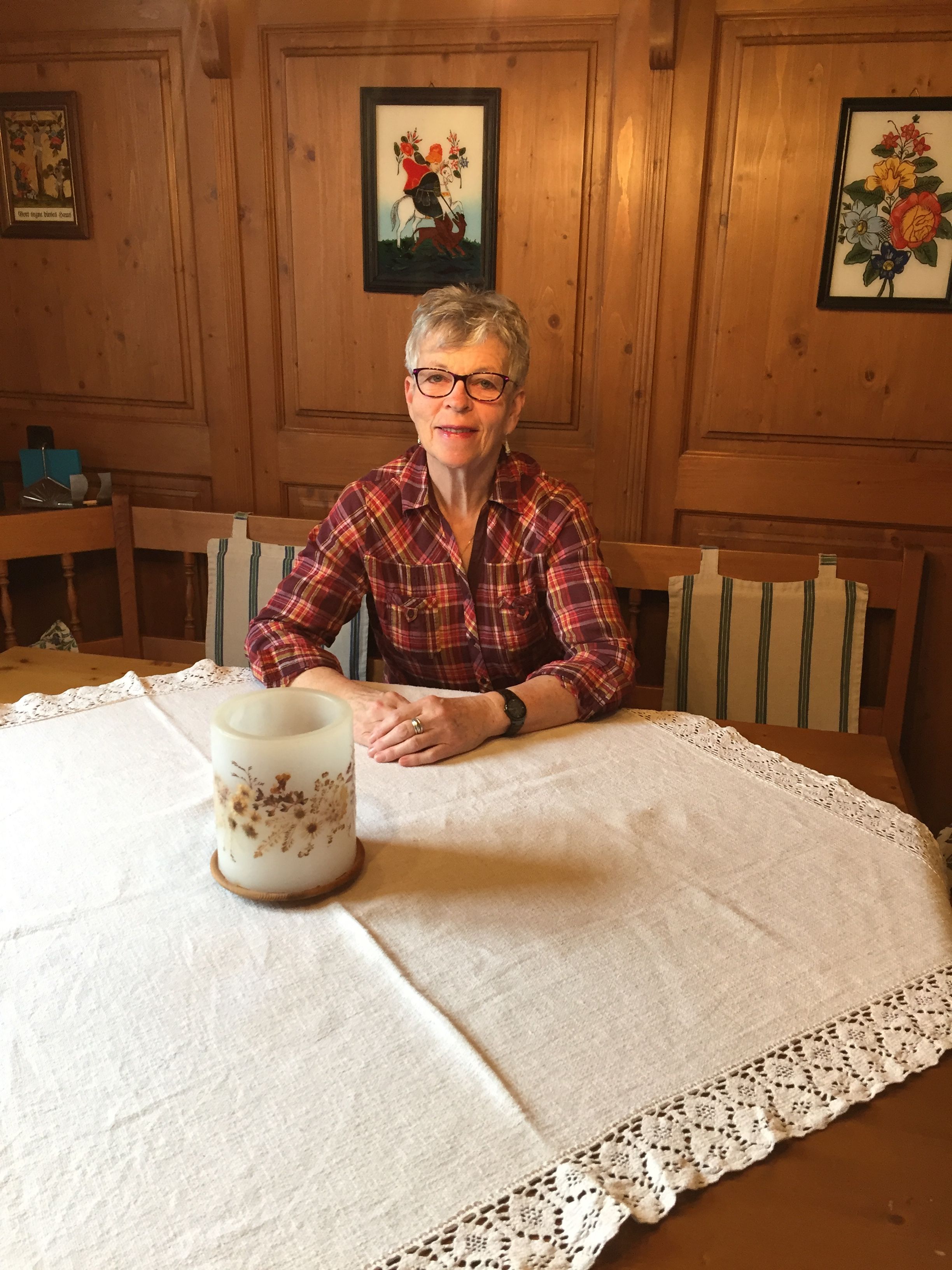 Eine Frau sitzt an einem Tisch mit weißer Tischdecke in einem holzgetäfelten Raum.