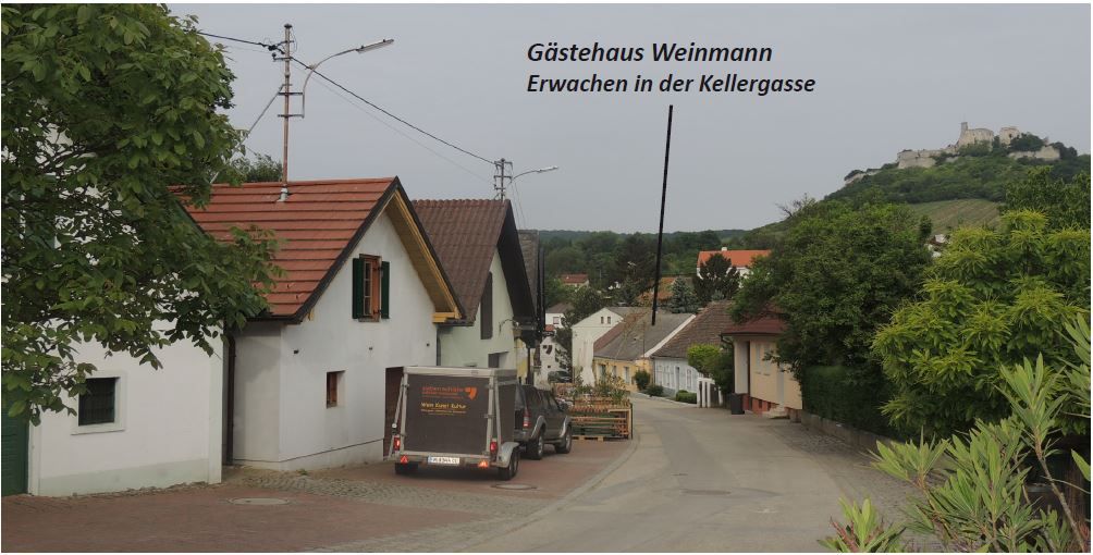 Eine malerische Straße mit traditionellen Häusern und einem Anhänger. Im Hintergrund ist eine Burg auf einem Hügel zu sehen.