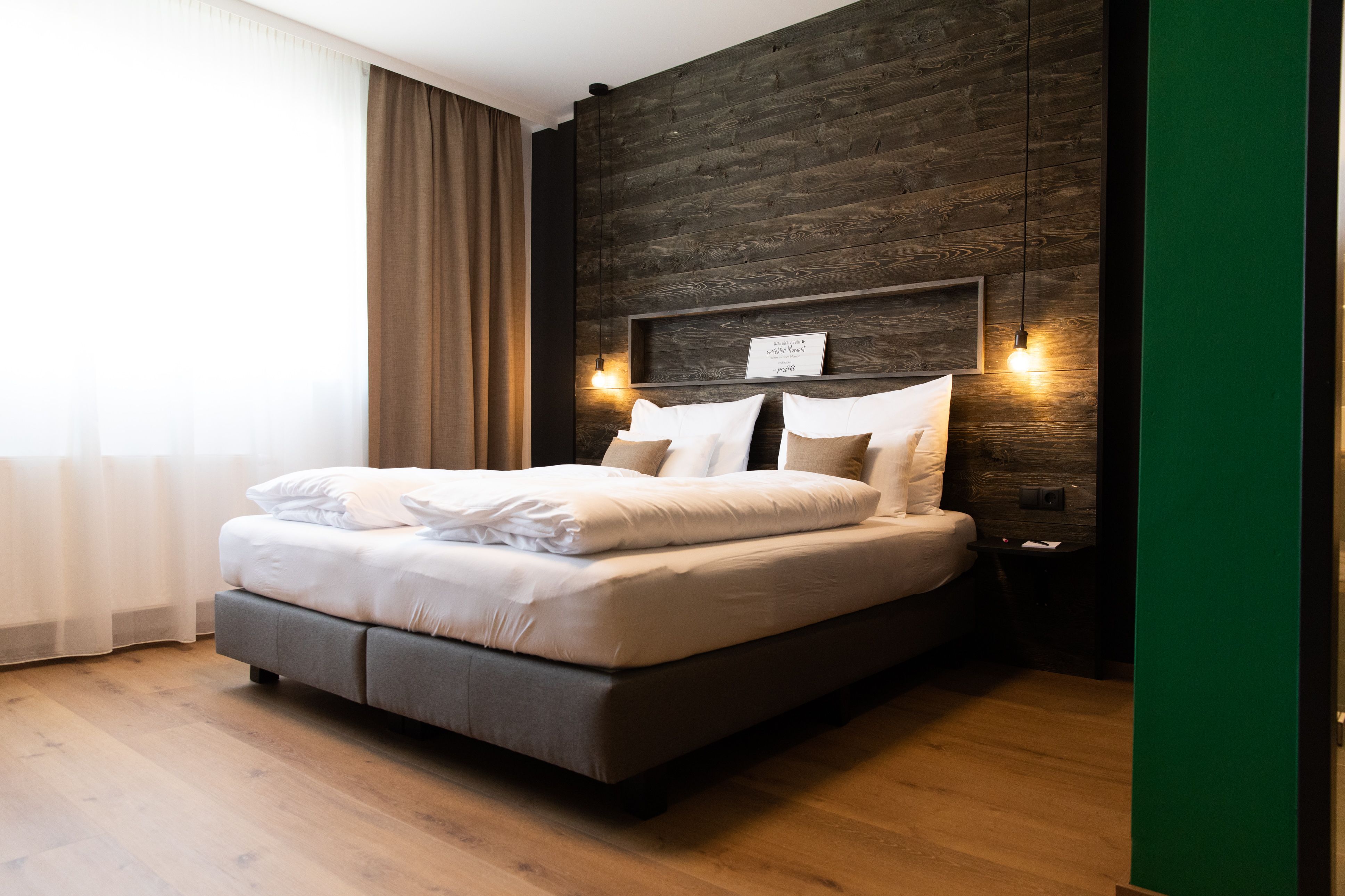 Modernes Hotelzimmer mit großem Bett, Holzwand und hängenden Lampen.