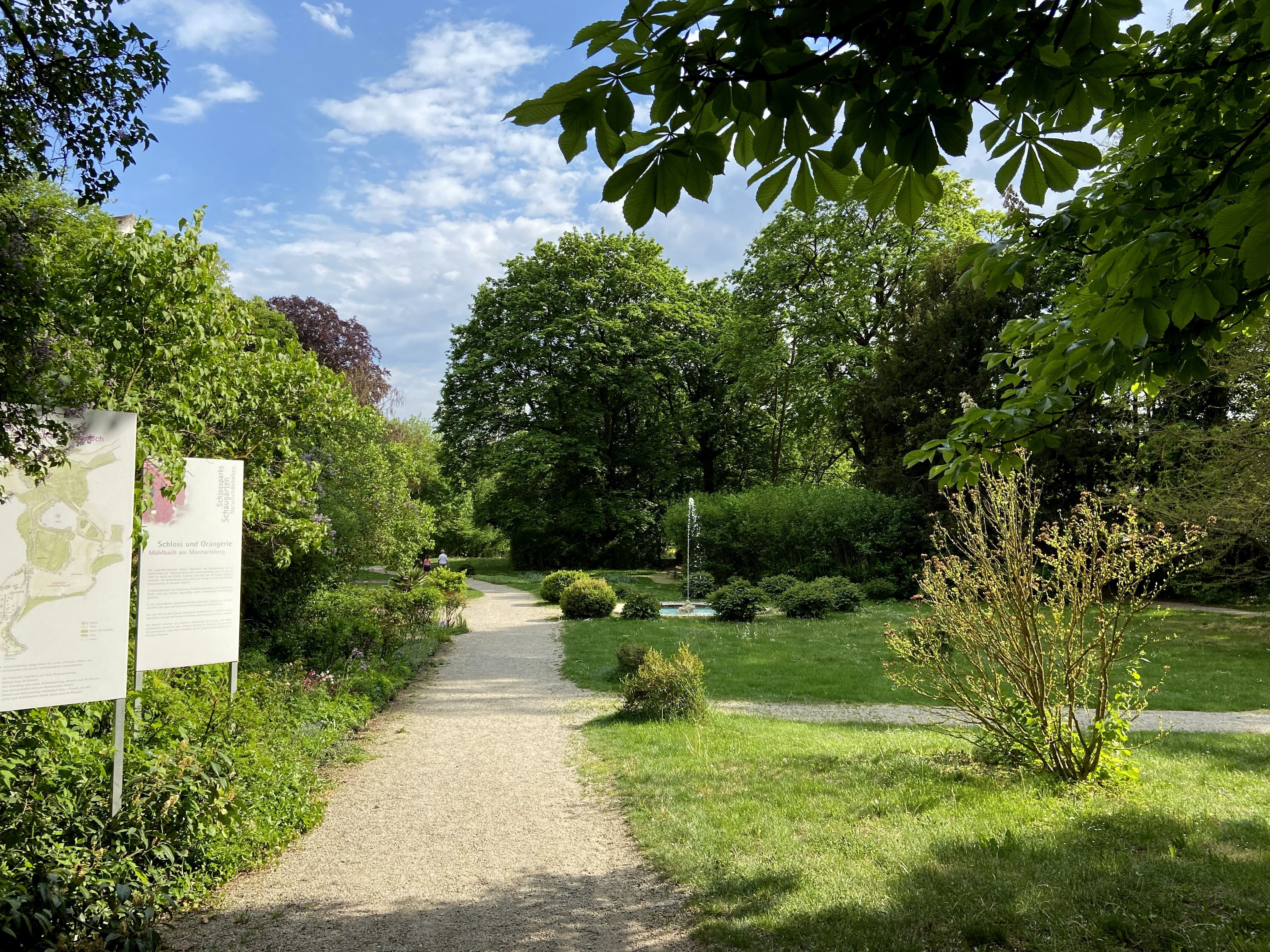 Eingang zum Schlosspark in Mühlbach mit Weg und Schildern.