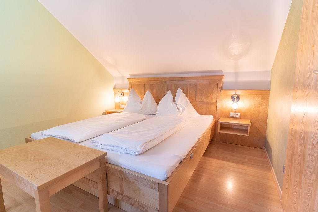 Gemütliches Schlafzimmer mit Holzmöbeln und Doppelbett unter einer Dachschräge.