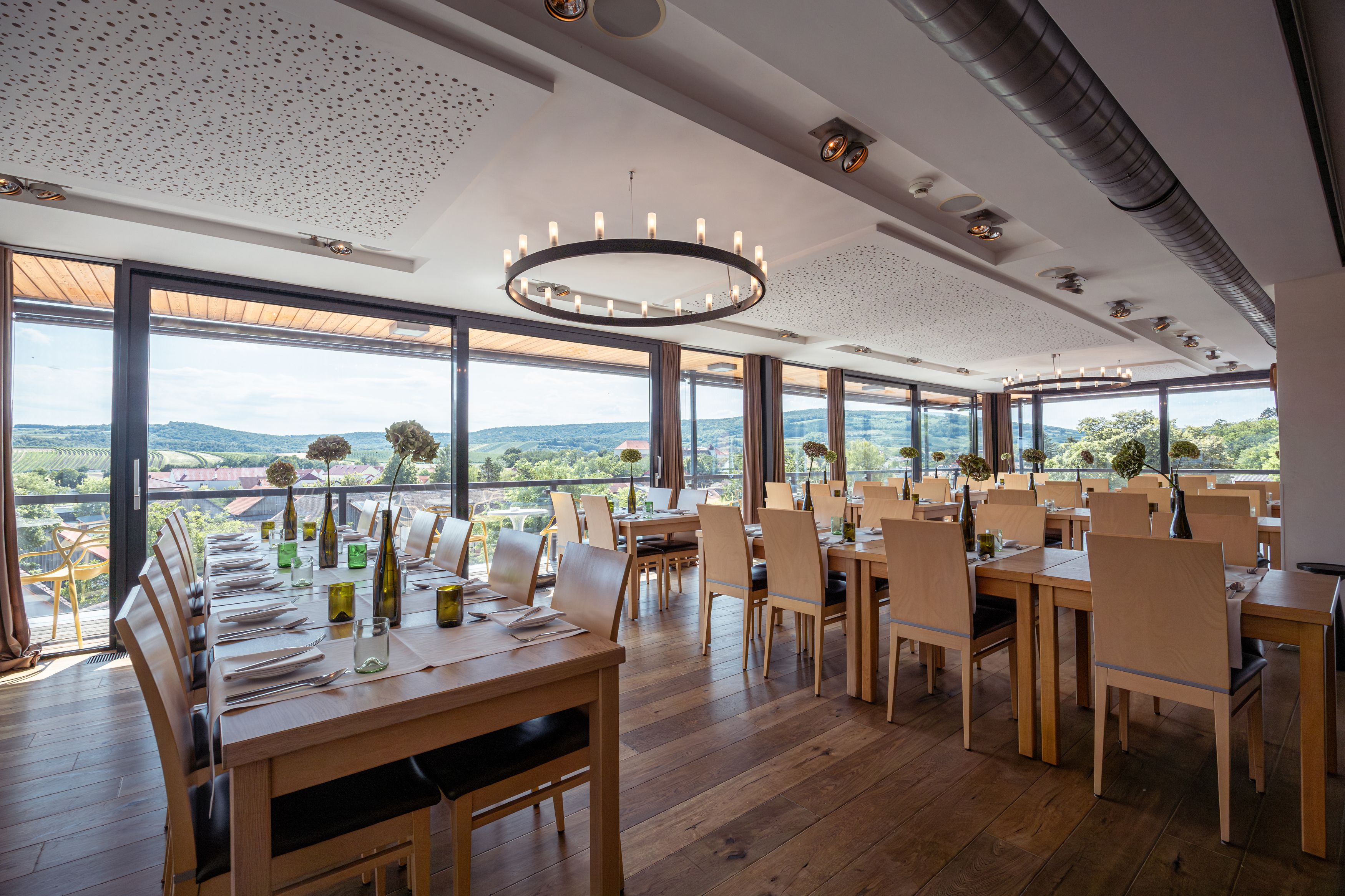 Innenansicht eines modernen Restaurants mit großen Fenstern und Blick auf Weinberge.