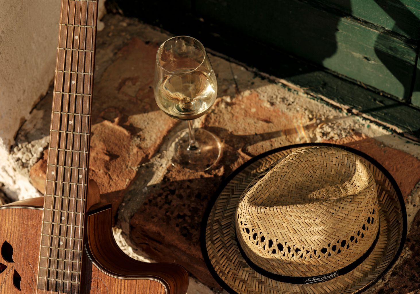Vor einer Kellertür liegen eine Gitarre, ein Weinviertel Hut und ein Weinglas gefüllt mit Weißwein. 