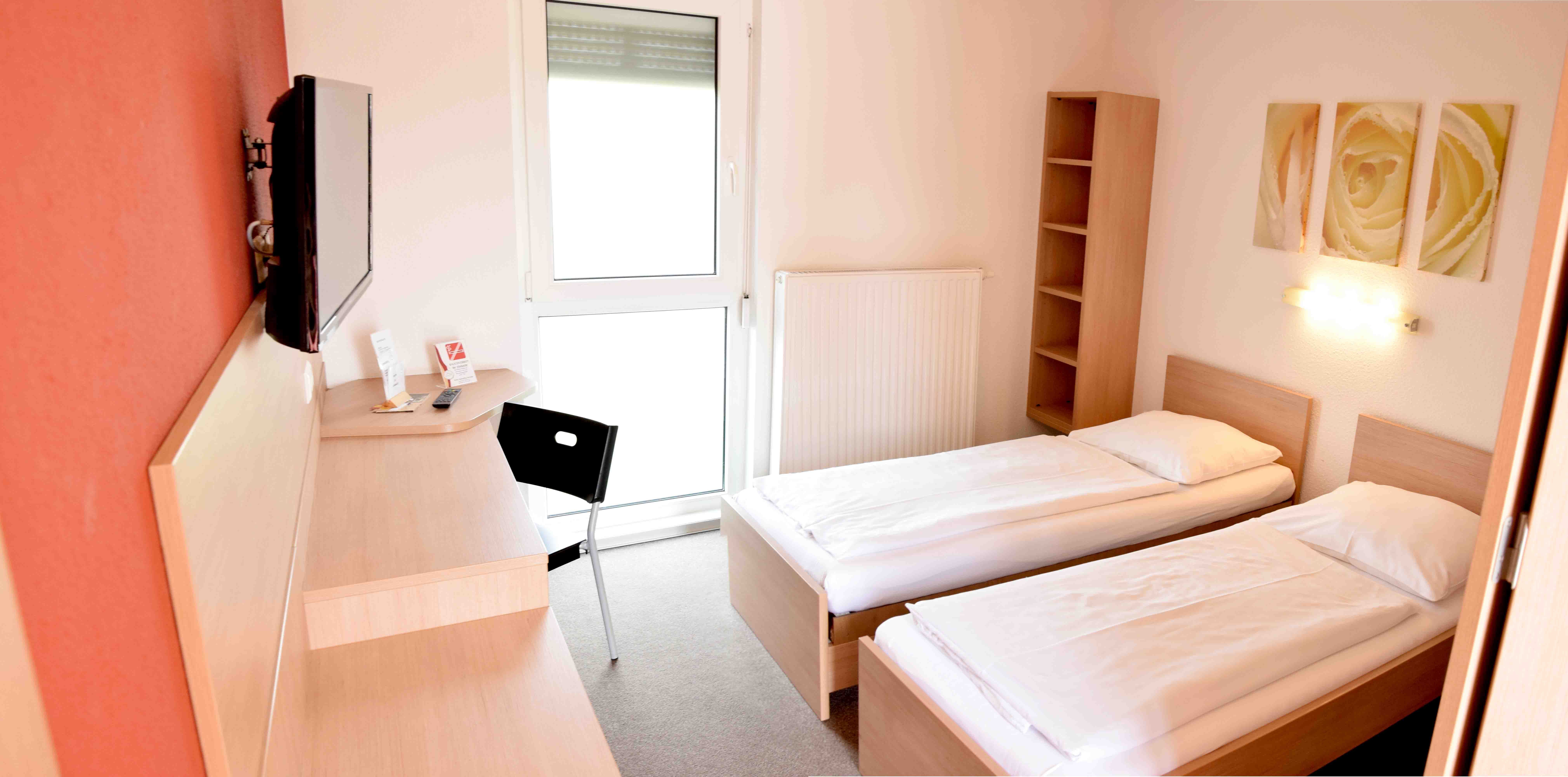 Ein einfaches Motelzimmer mit zwei Einzelbetten, einem Schreibtisch, einem Stuhl und einem Fernseher an der Wand.