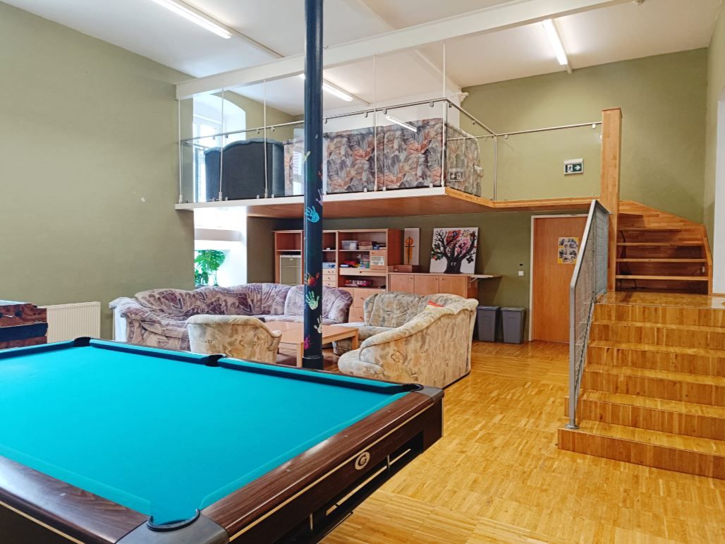Miestnosť pre mladých s biliardovým stolom, pohovkami a galériou so schodiskom.