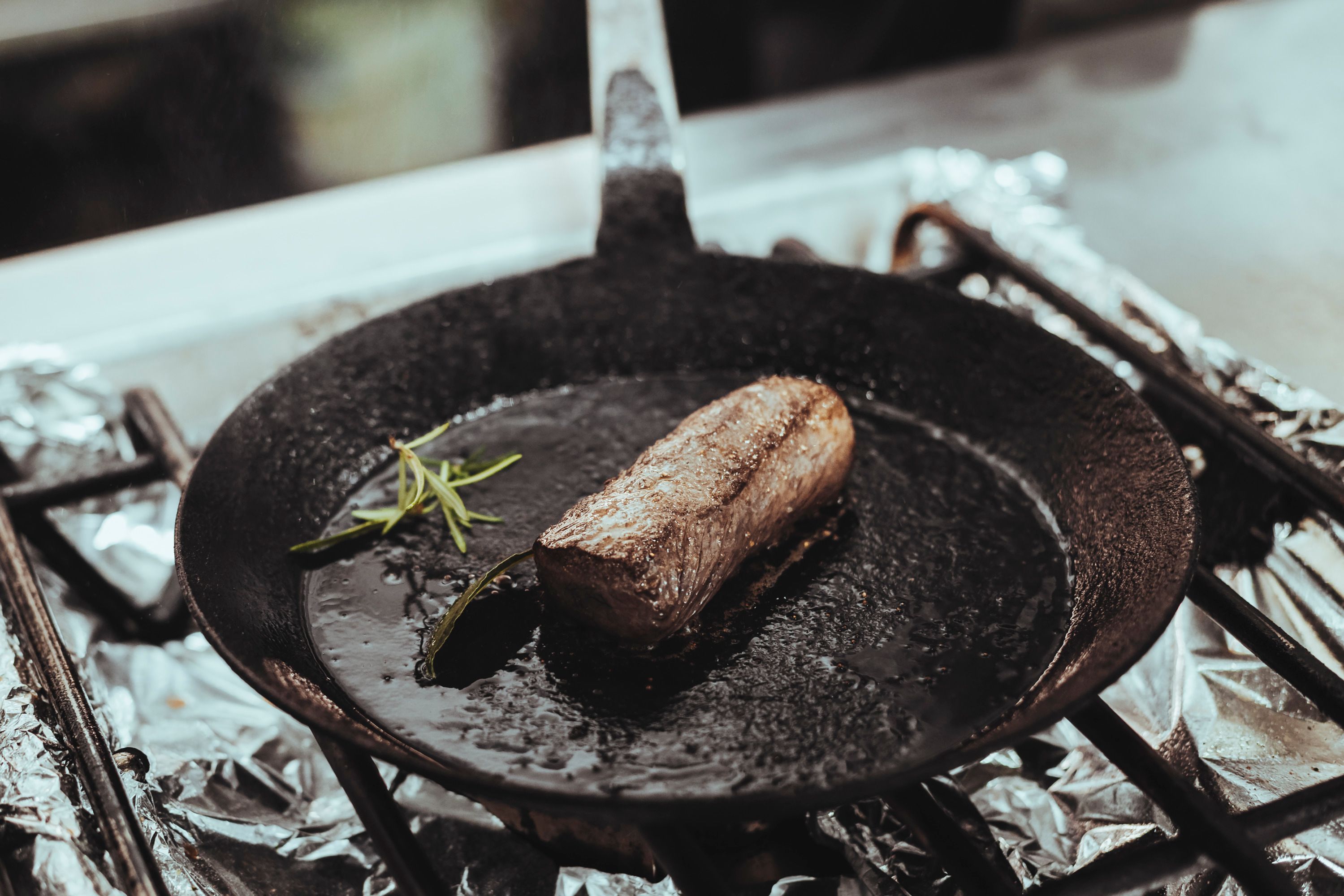 Ein Stück Fleisch brät in einer gusseisernen Pfanne mit Rosmarin.