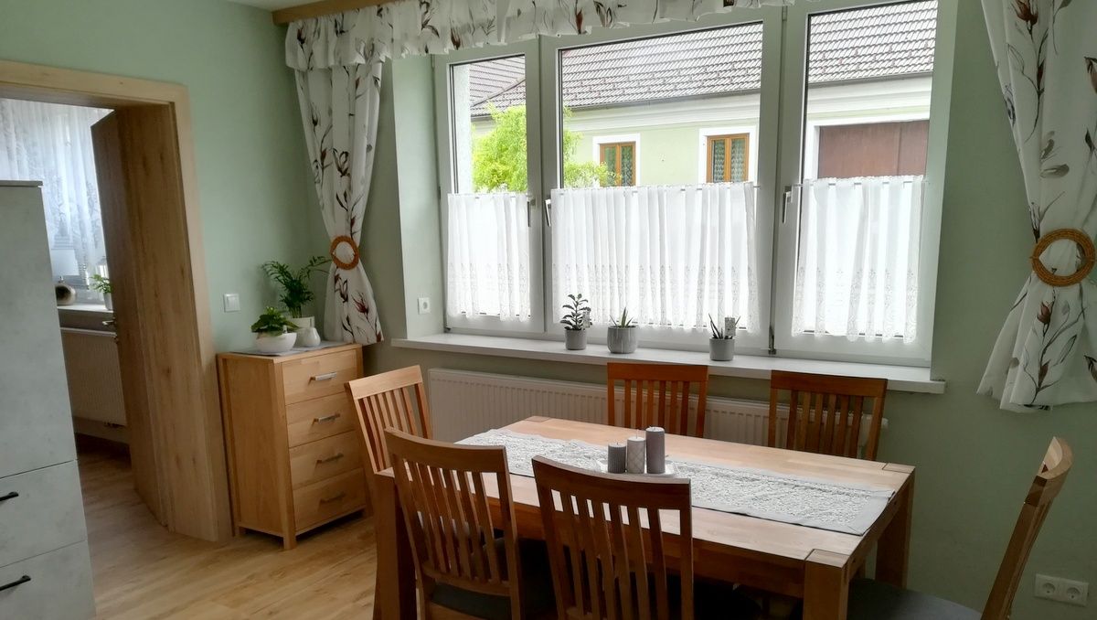 Esszimmer mit Holztisch, Stühlen und Pflanzen auf der Fensterbank.