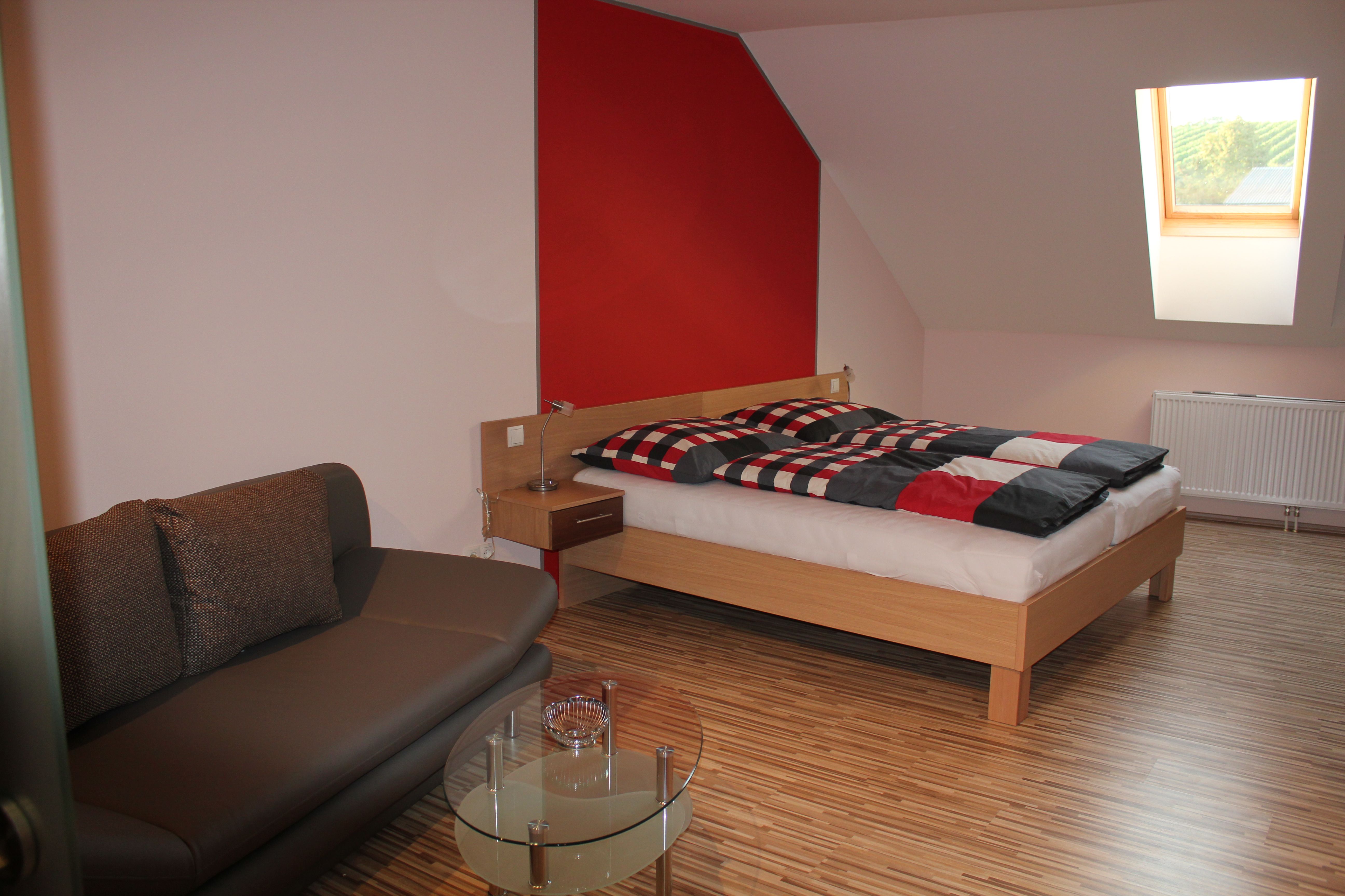 Modern eingerichtetes Gästezimmer mit Bett, Sofa und Dachfenster.