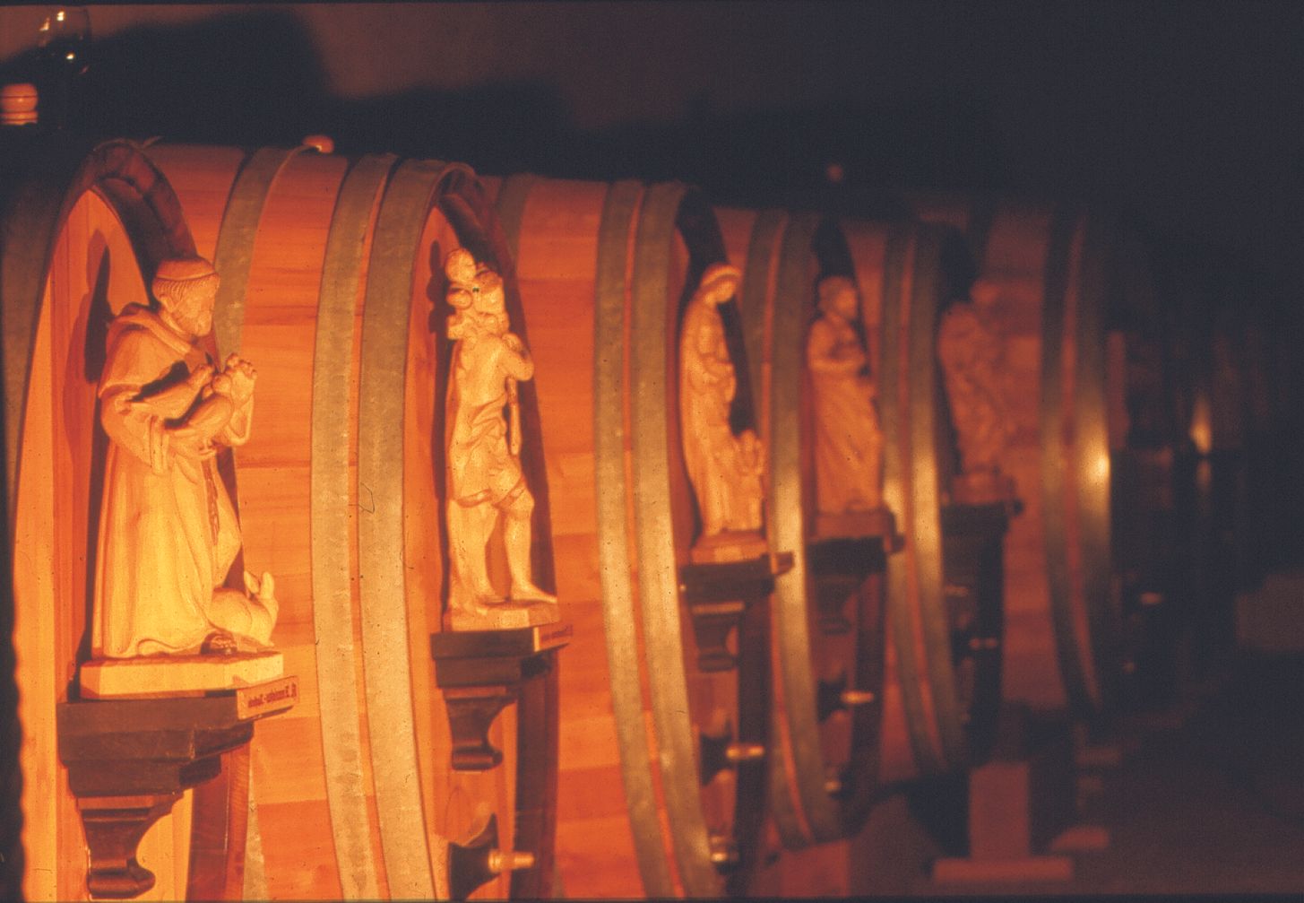 Reihe von Holzfässern mit geschnitzten Figuren in einem Weinkeller.