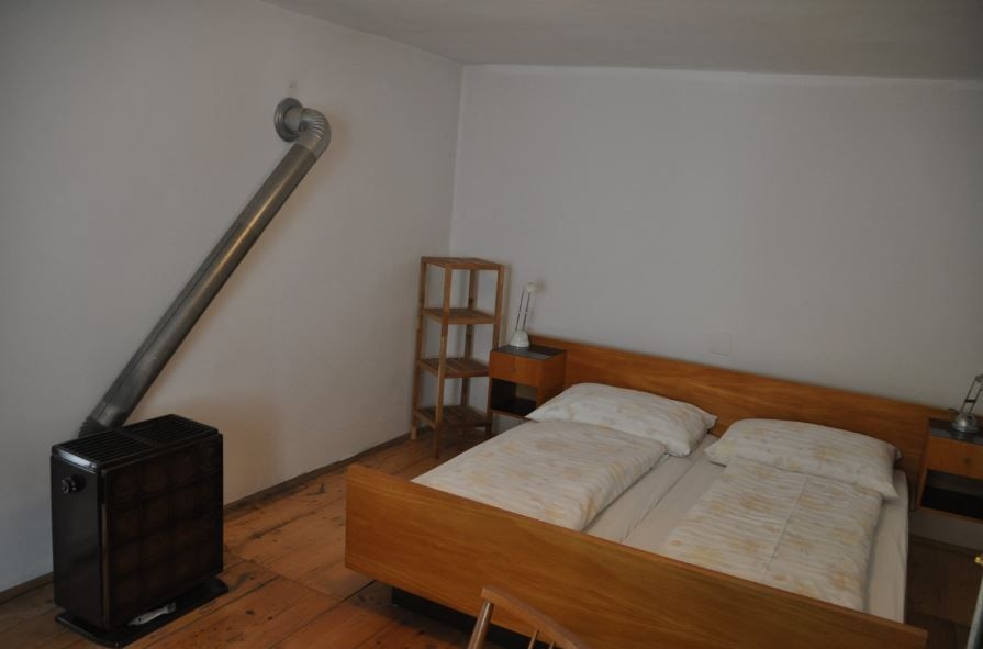 Ein einfach eingerichtetes Schlafzimmer mit Doppelbett, Nachttischen, Regal und Ofen.