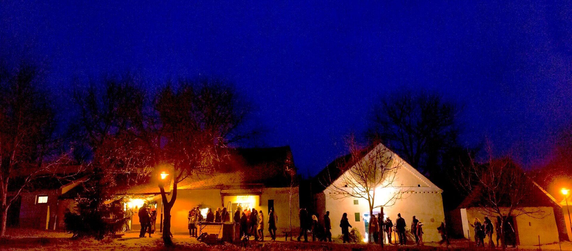 In der kühlen Abenddämmerung versammeln sich Menschen vor den beleuchteten Gebäuden, während die warmen Lichter eine einladende Atmosphäre schaffen. Der Duft von Glühwein und frisch gebackenem Gebäck liegt in der Luft und verspricht ein unvergessliches Erlebnis in der besinnlichen Zeit des Jahres.