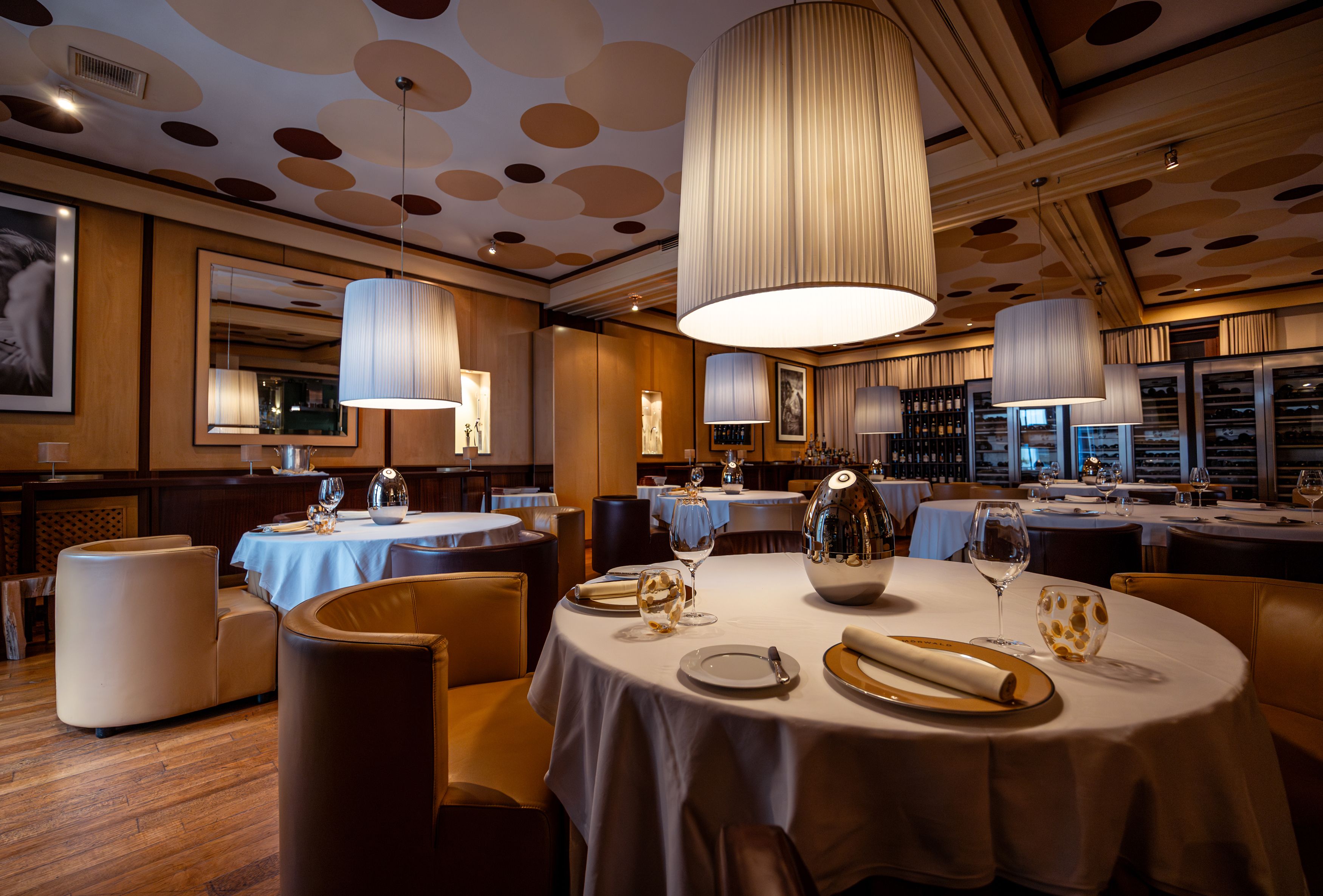 Elegantes Restaurant mit runden Tischen, weißen Tischdecken und großen, hängenden Lampen.