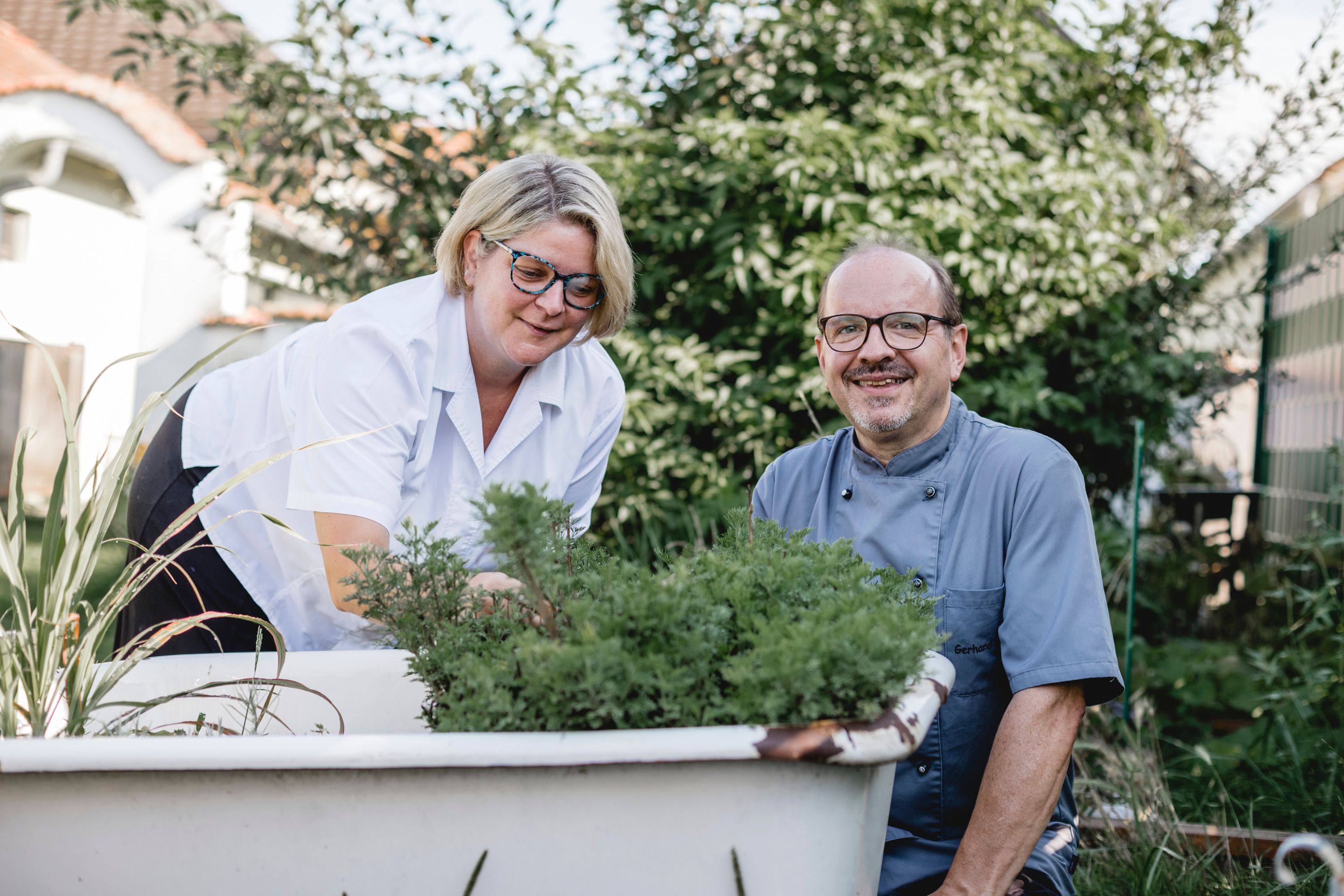 Zwei Personen gärtnern in einer alten Badewanne im Freien.