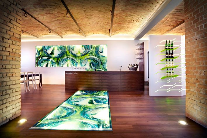 Modernes Weingut-Interieur mit beleuchtetem Boden und Weinflaschen an der Wand.