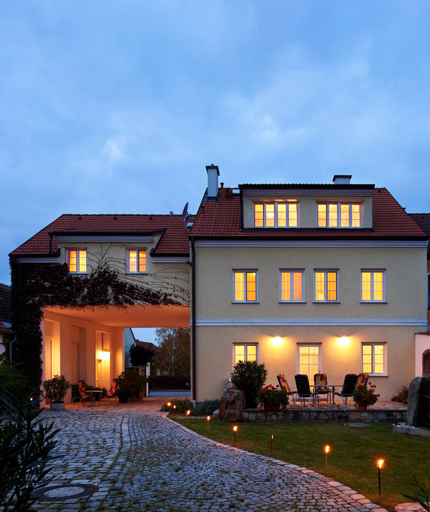 Beleuchtetes Gebäude mit gepflastertem Weg und Gartenmöbeln im Vordergrund.