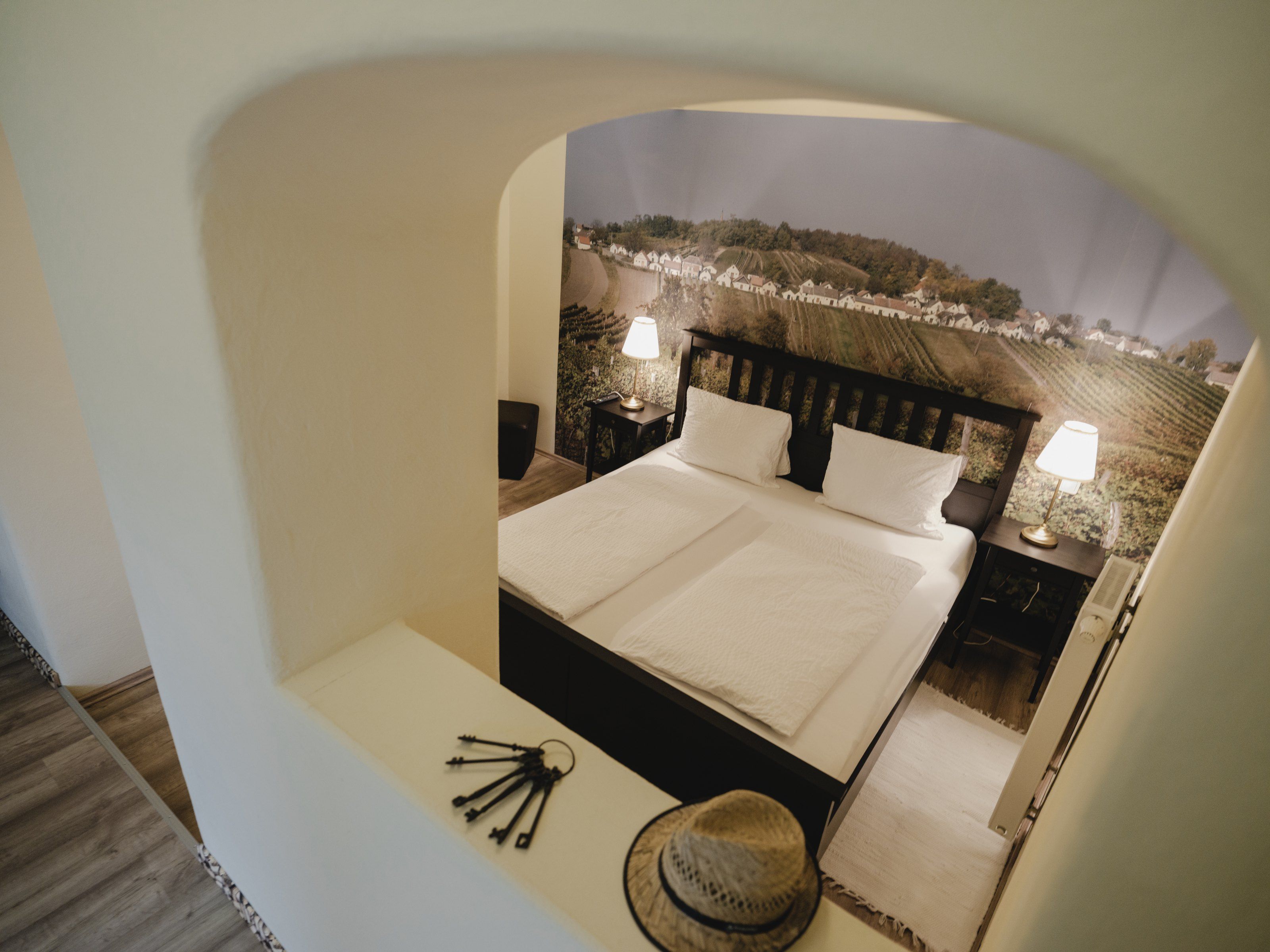 Ein gemütliches Schlafzimmer mit Doppelbett, zwei Nachttischlampen und einer Wandtapete mit Weinlandschaft.