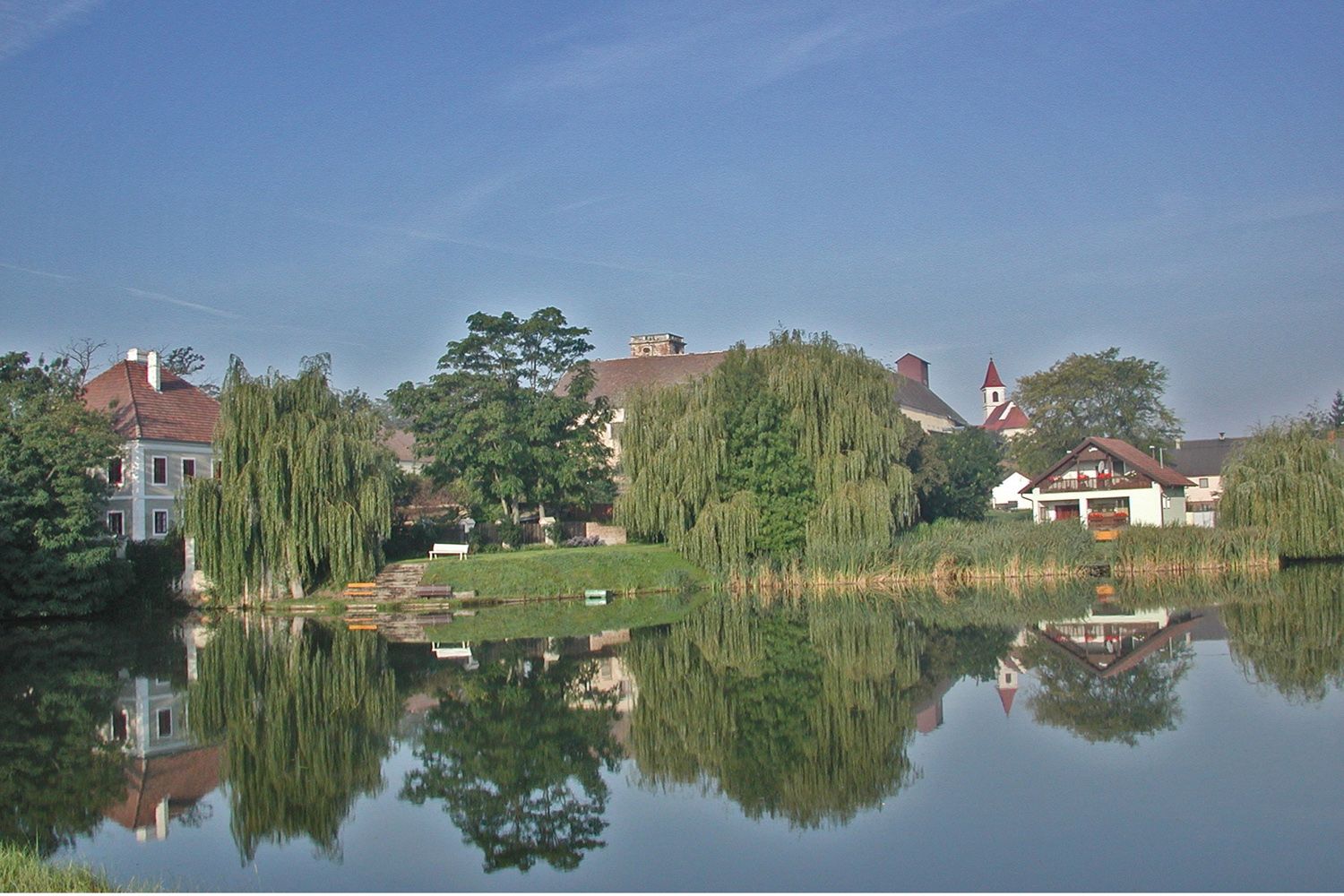 Ein ruhiger Teich mit Spiegelung von Bäumen und Gebäuden in Niederabsdorf.