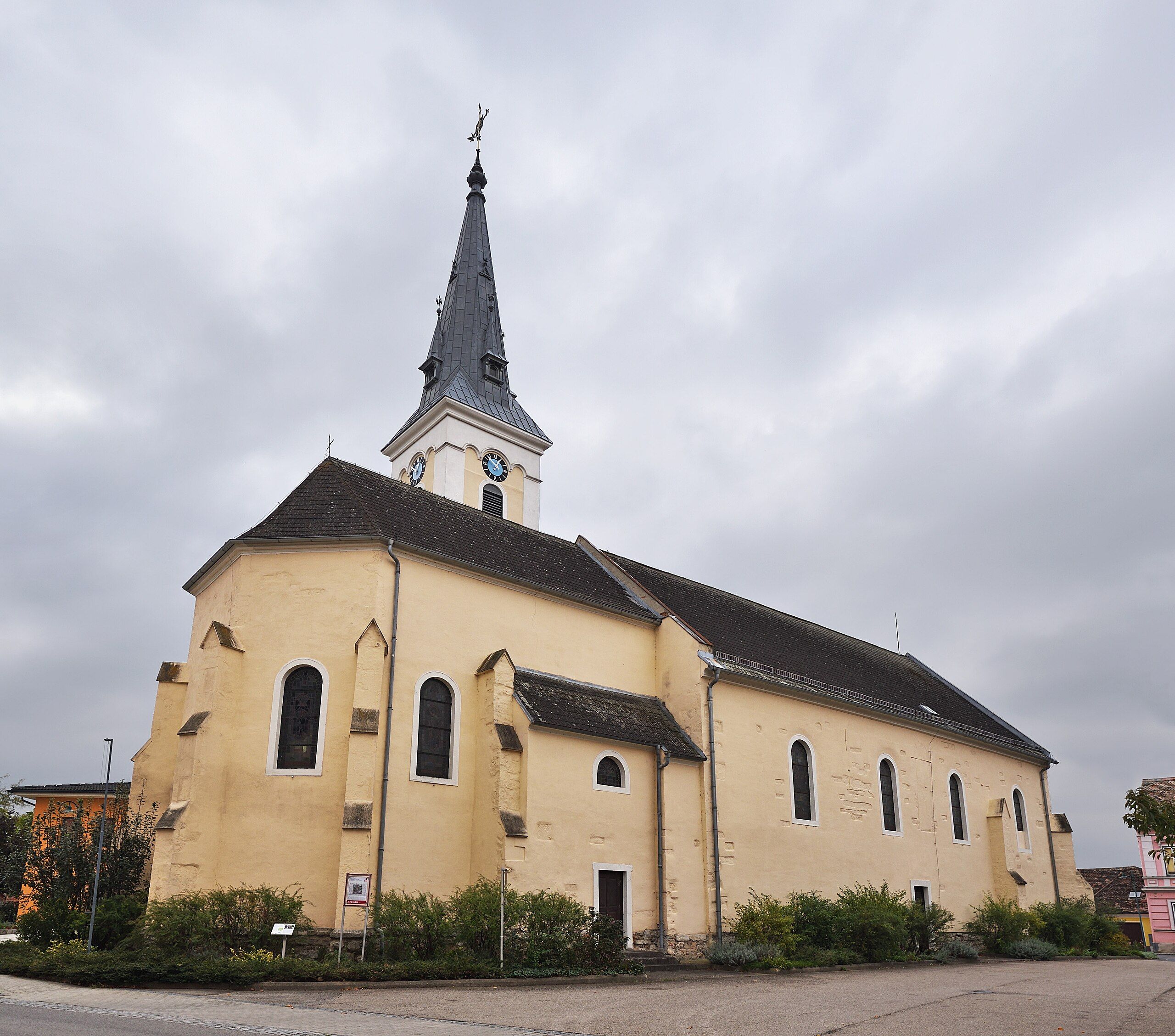 A yellow church with a tower and a clock against a cloudy sky.