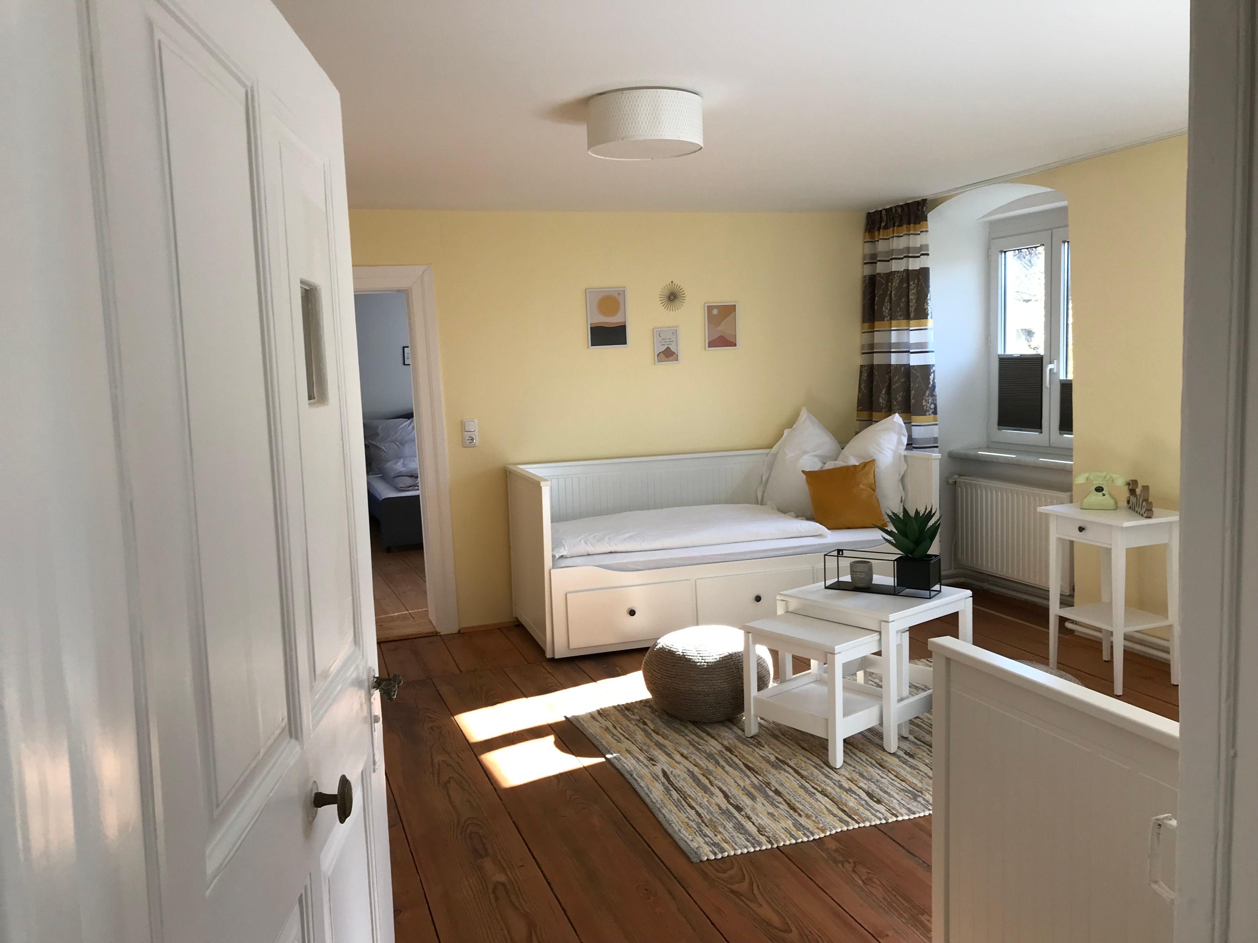 Bright room with yellow walls, a white day bed, small table and plants.