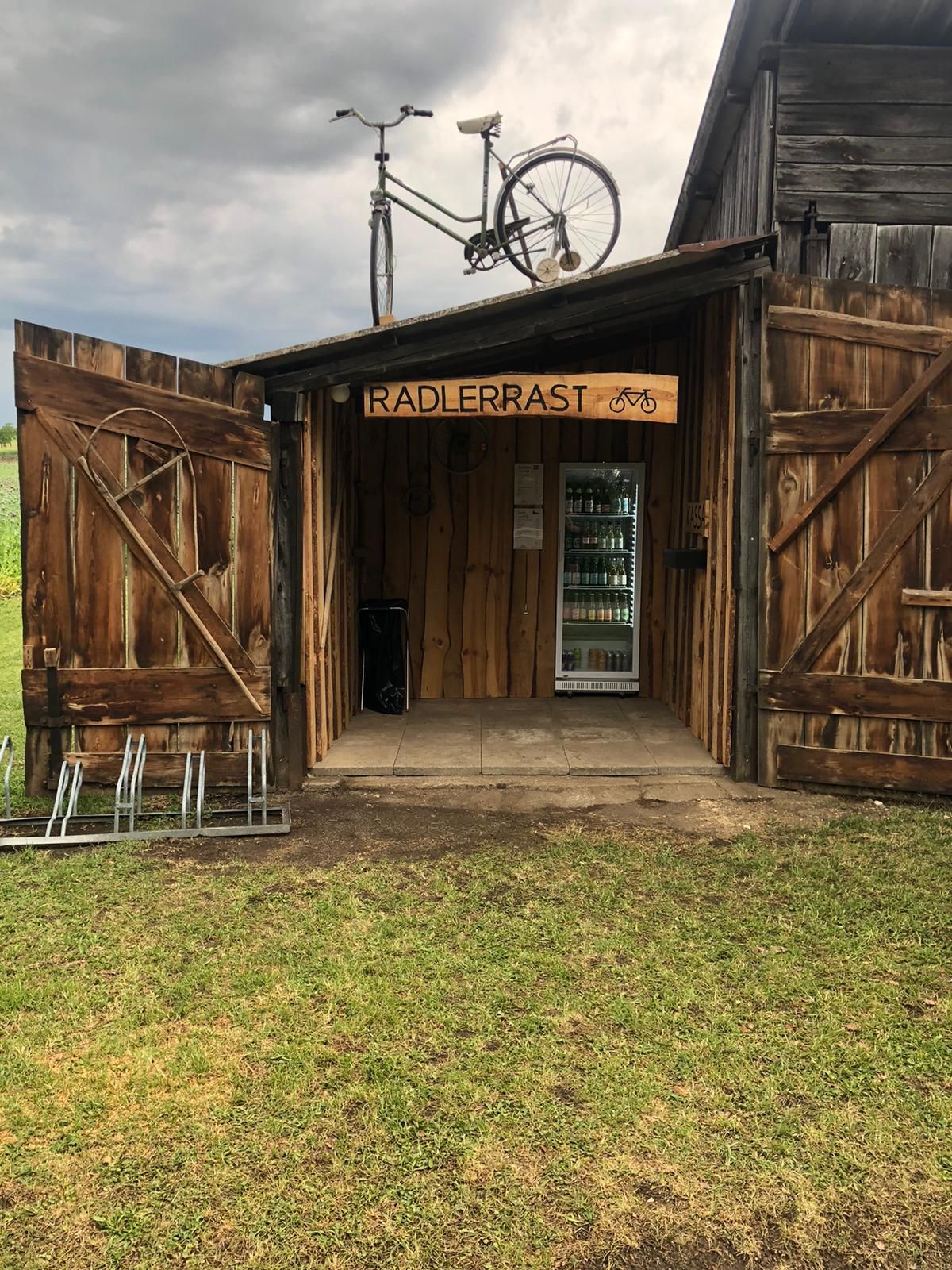 Holzhütte mit Schild 'Radlerrast', Fahrrad auf dem Dach, Getränke im Inneren.