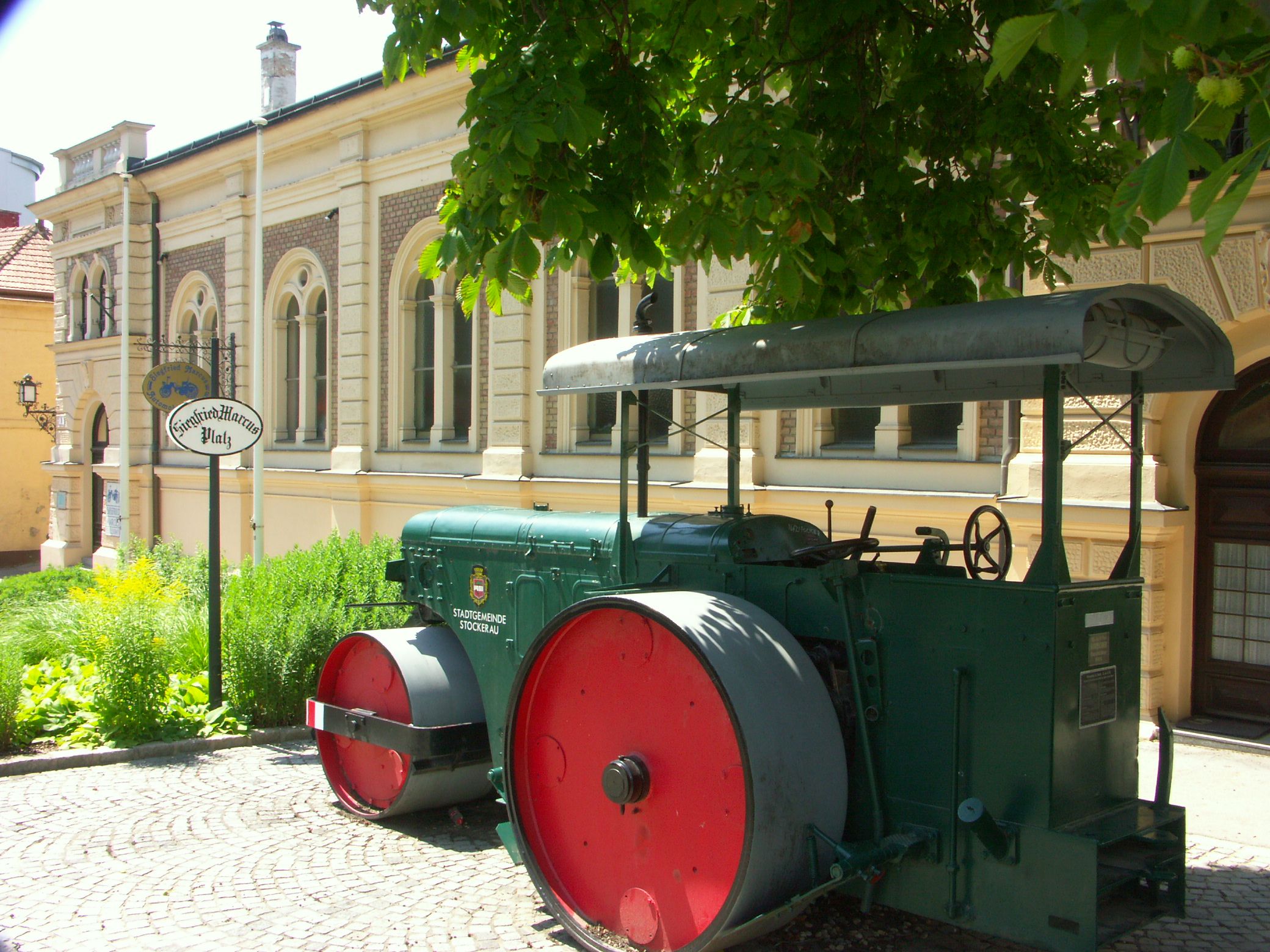 Historic steamroller in front of a building with the inscription 'Siegfried Marcus Platz'.