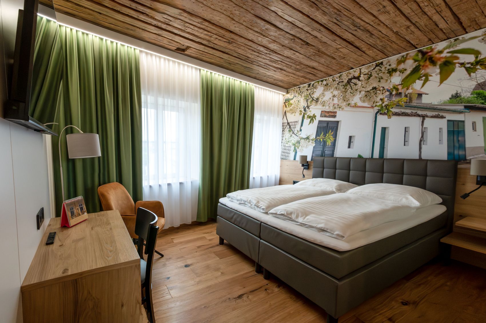 Modernes Gästezimmer mit Doppelbett, Holzboden und grünen Vorhängen.