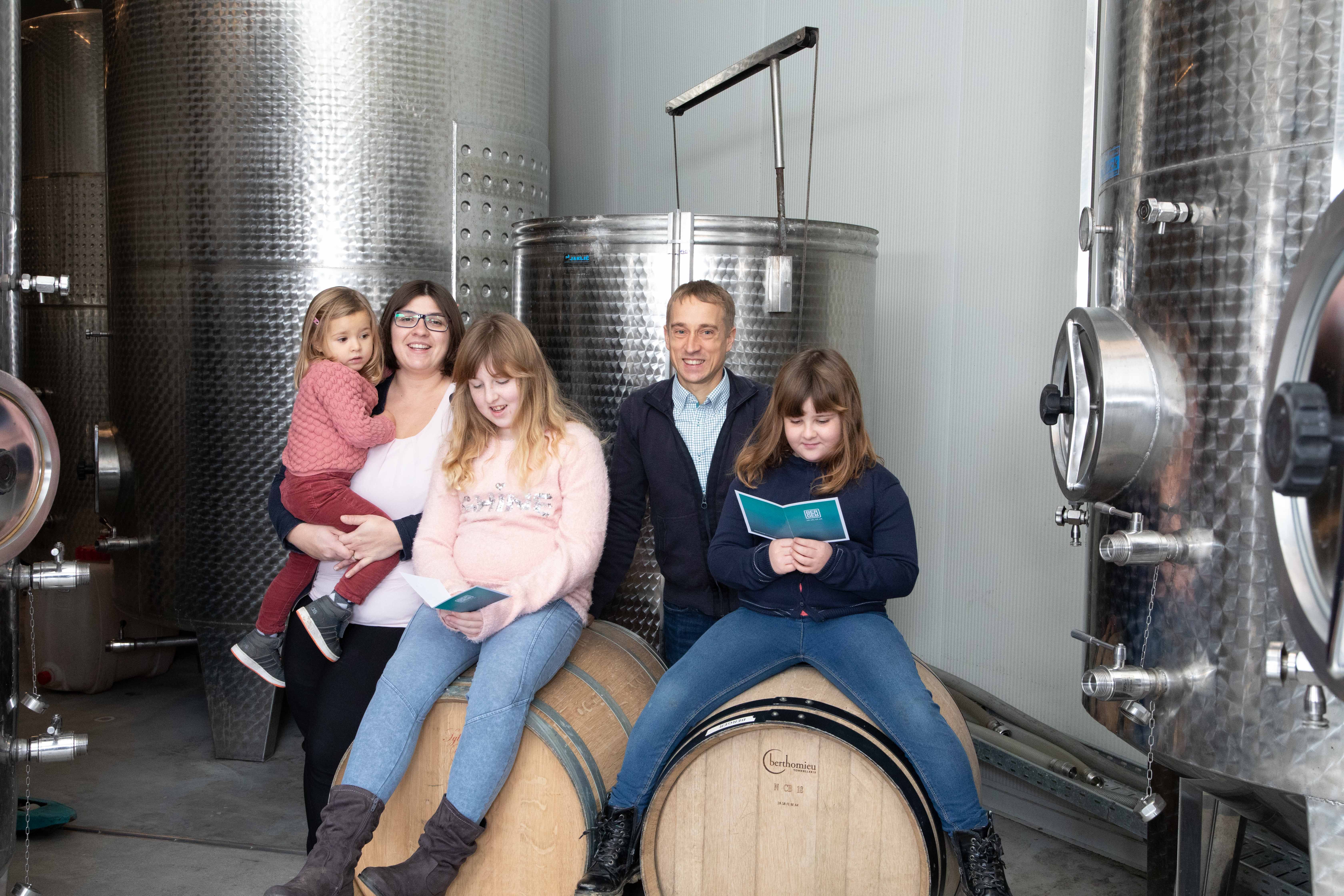A family poses in front of large stainless steel tanks in a winery.