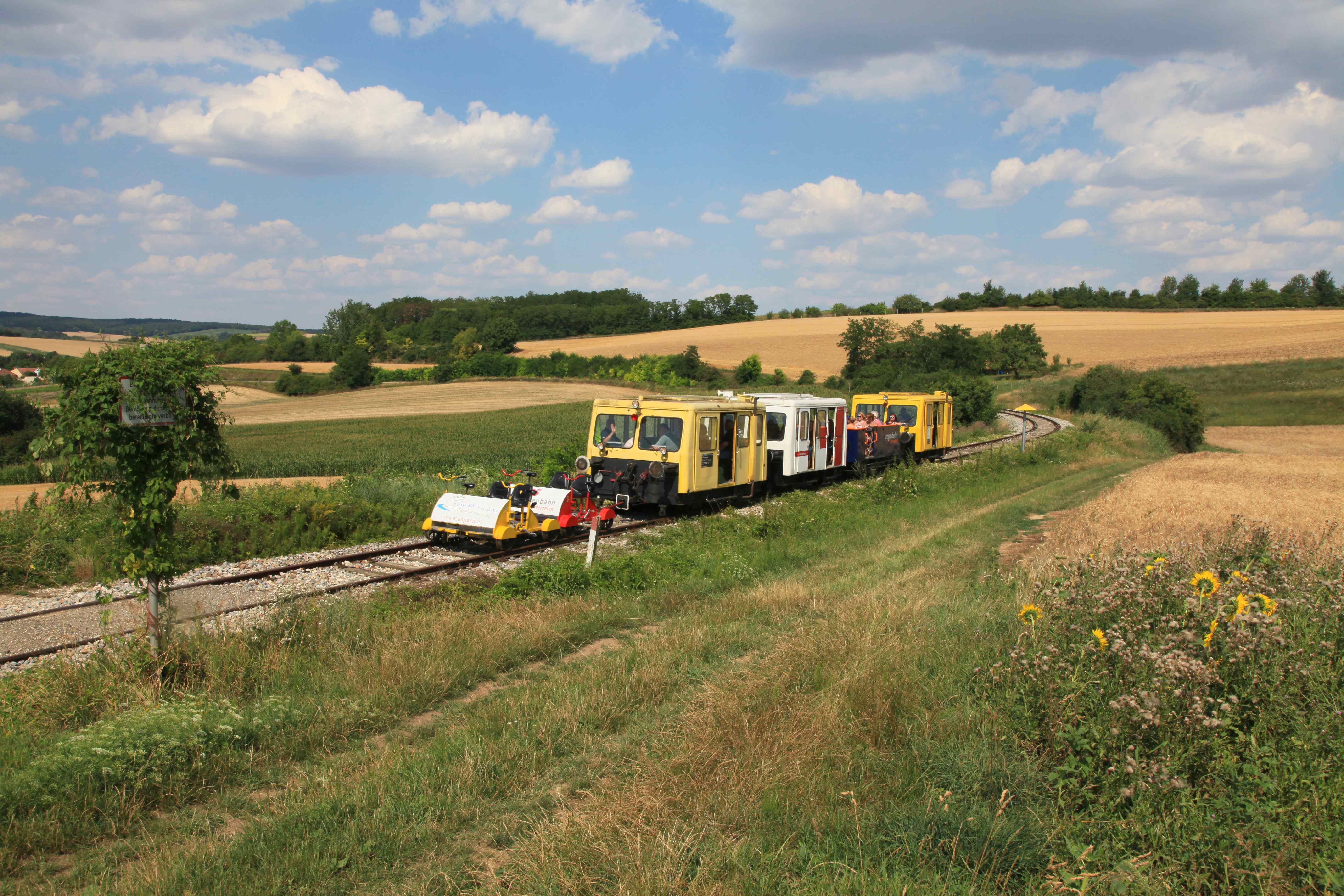 Draisinen auf einer ländlichen Bahnstrecke in einer hügeligen Landschaft mit Feldern und Bäumen.
