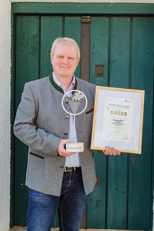 Person holding an award and a certificate in front of a green wooden door.