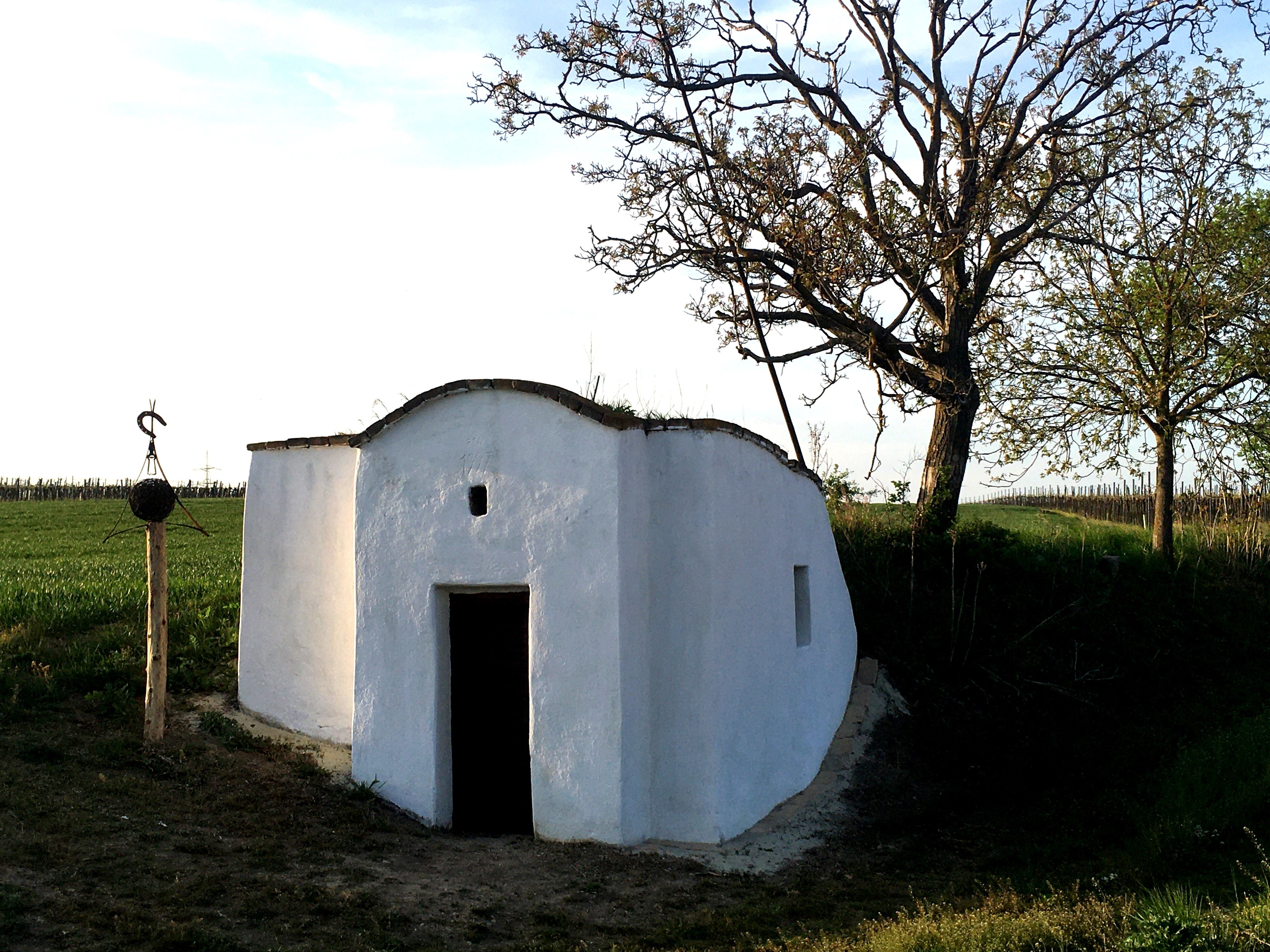 Weiße Hiatahütte auf einem Feld mit Bäumen und einem Holzpfosten daneben.