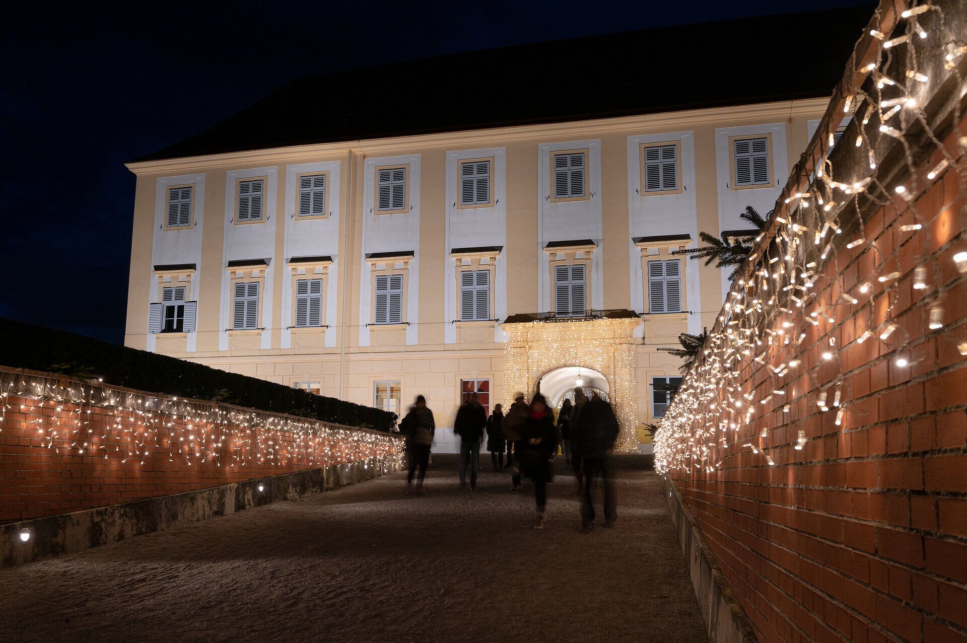 In der festlich beleuchteten Umgebung des Adventmarktes entfaltet sich eine zauberhafte Atmosphäre. Die sanften Lichter reflektieren sich in der kalten Winterluft und laden dazu ein, die Vorfreude auf Weihnachten zu genießen. Besucher schlendern gemütlich entlang der mit Lichtern geschmückten Wege und lassen sich von den festlichen Klängen verzaubern.