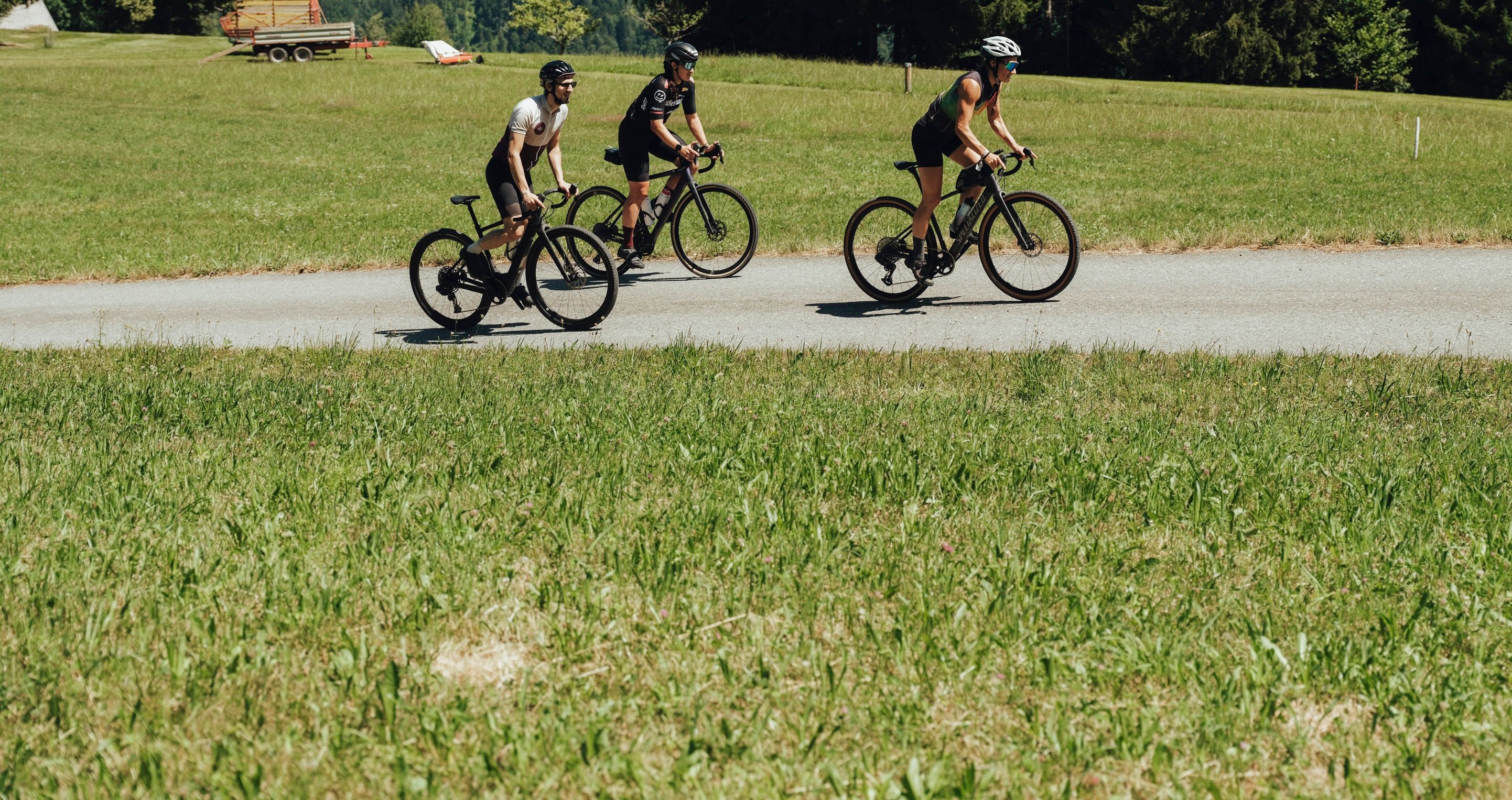 Drei Radfahrer auf einer ländlichen Straße in einer grünen Landschaft.